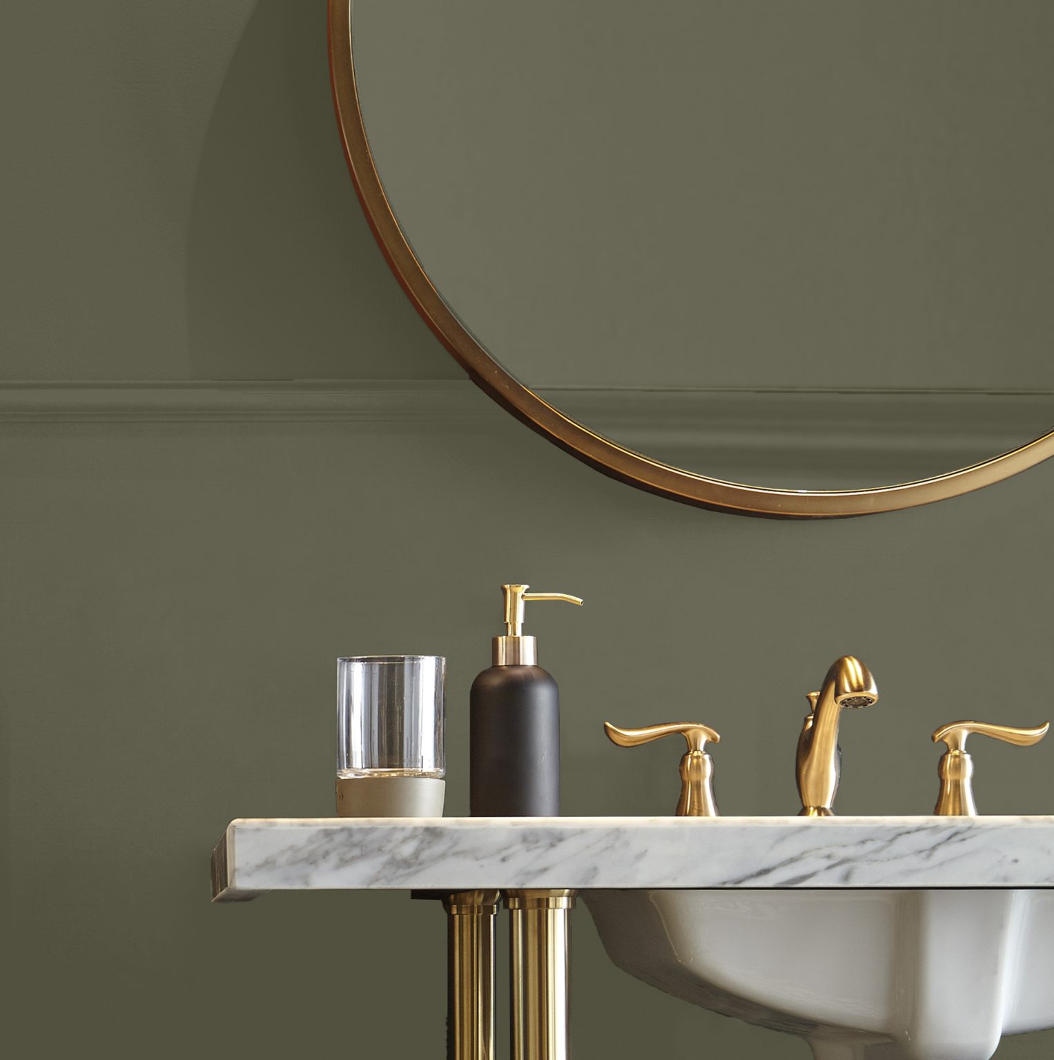 A closeup of a bathroom with the walls painted in a deep olive green and styled with gold hardware and décor