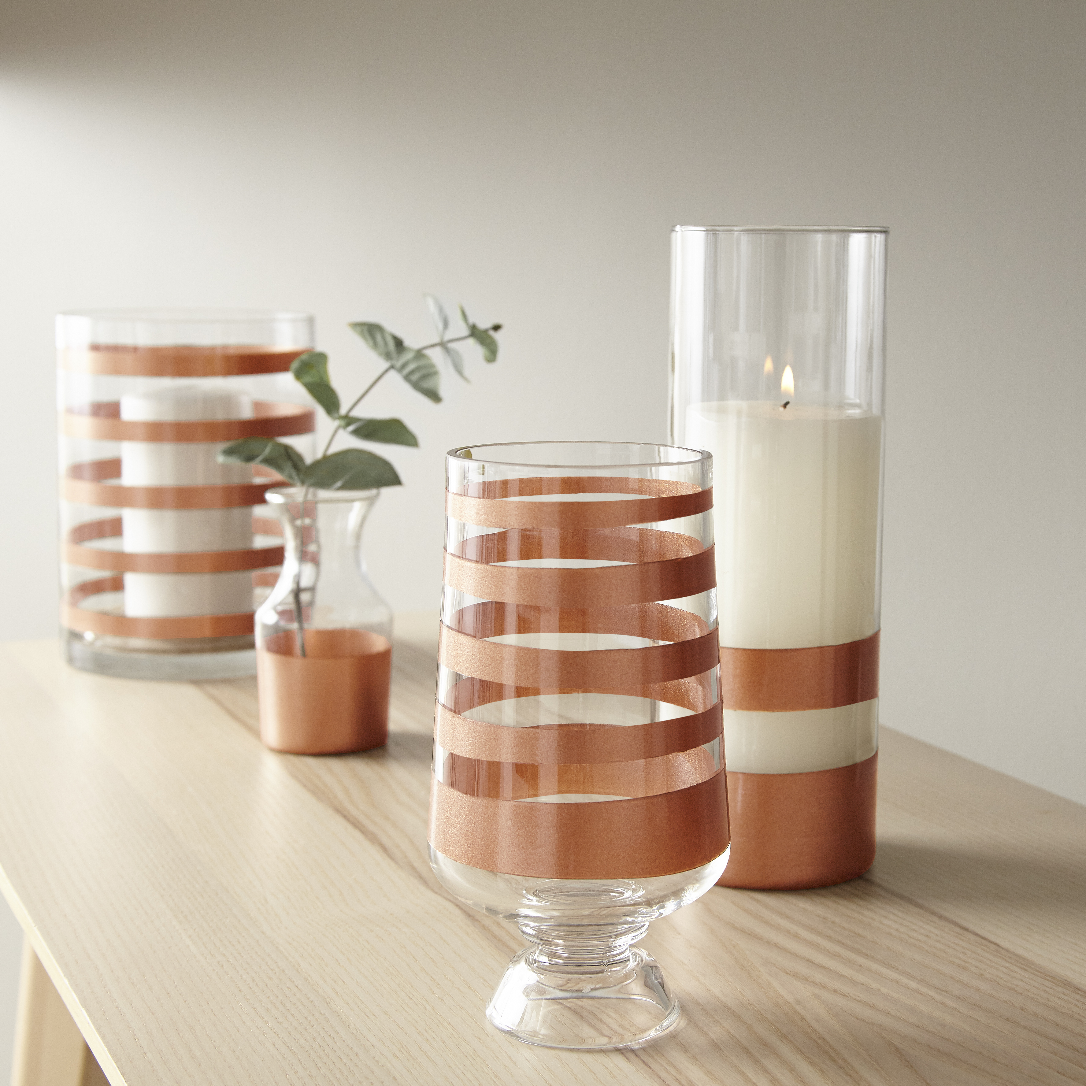 Four clear vases with spray painted striped designs in a metallic copper colour