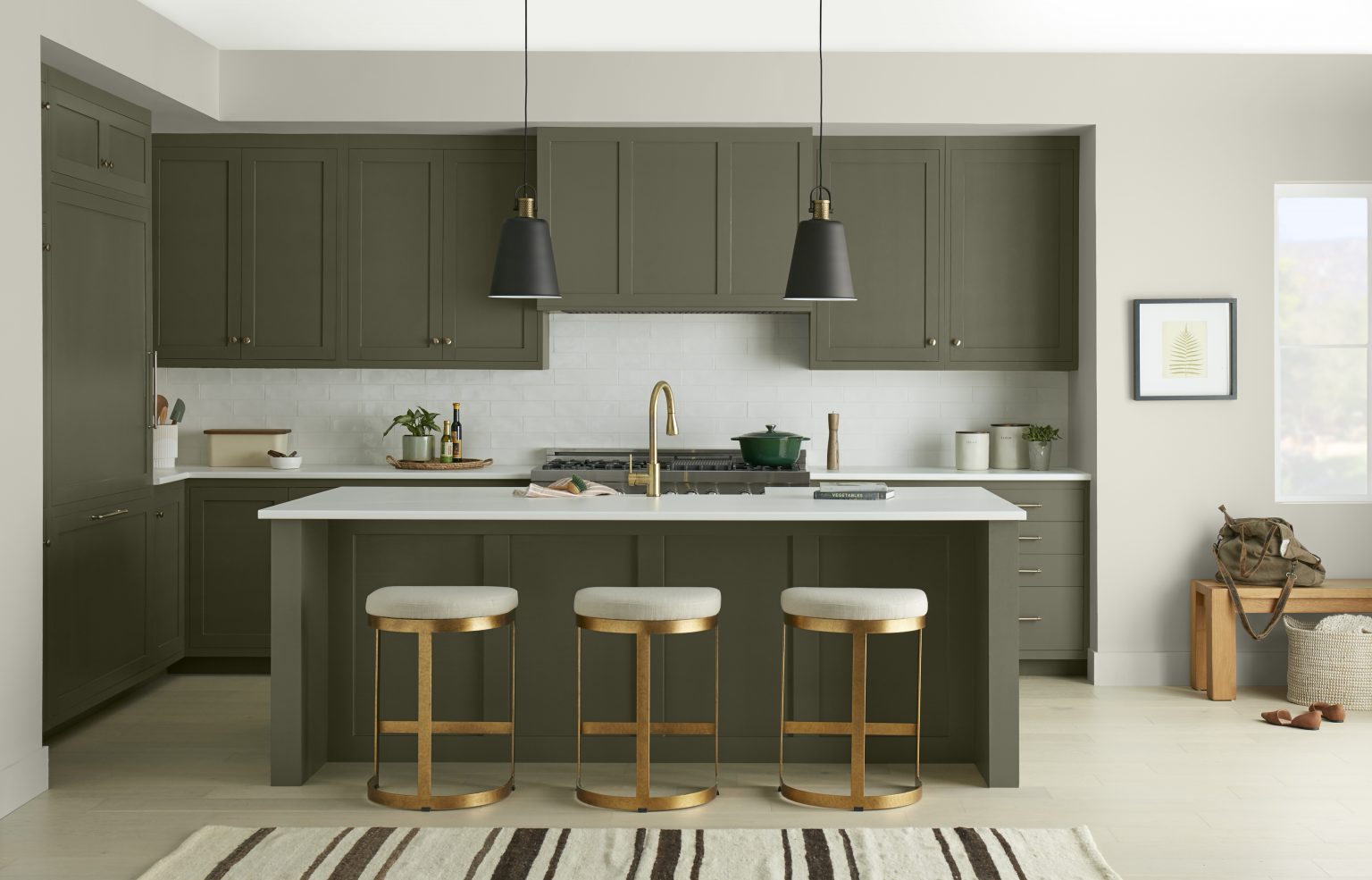 A modern kitchen with dark olive green cabinetry and a matching island, with hardware and kitchen bar stools in gold to match