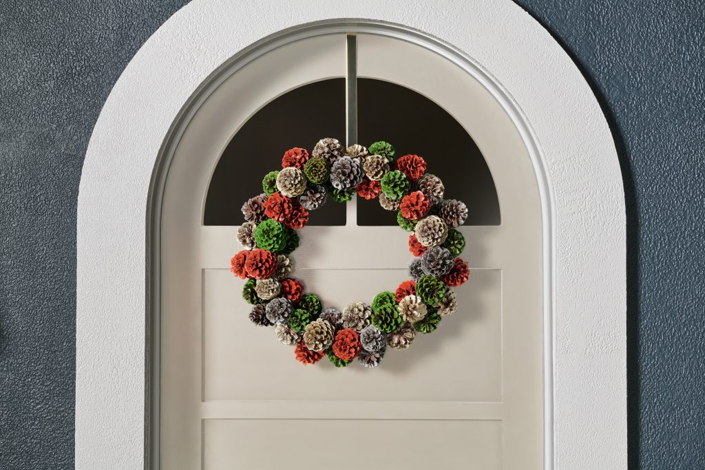 A closeup of a white exterior door with a spray-painted pinecone wreath