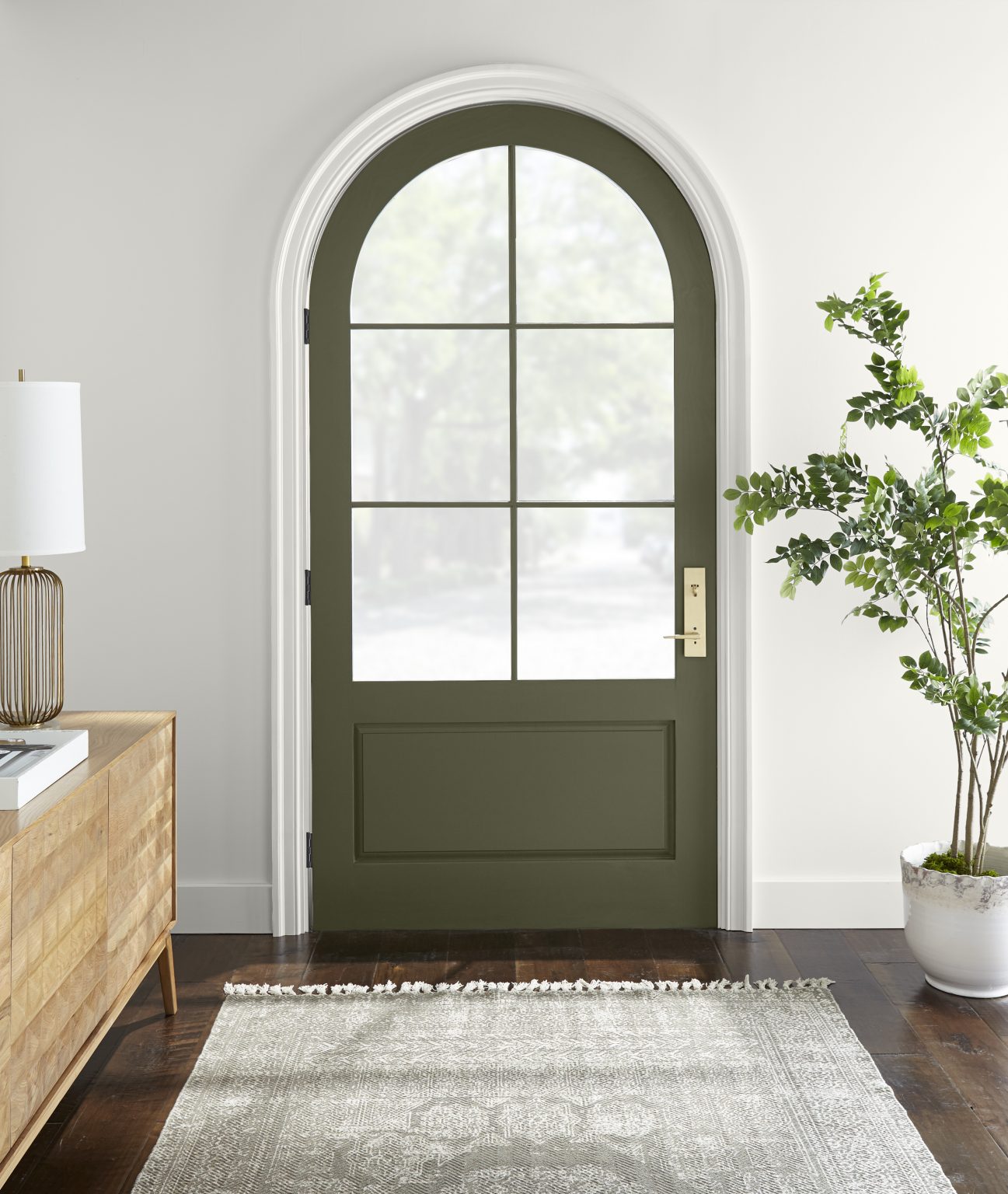 A white entryway with a green arched door, styled with a wood console table, neutral rug, and plant