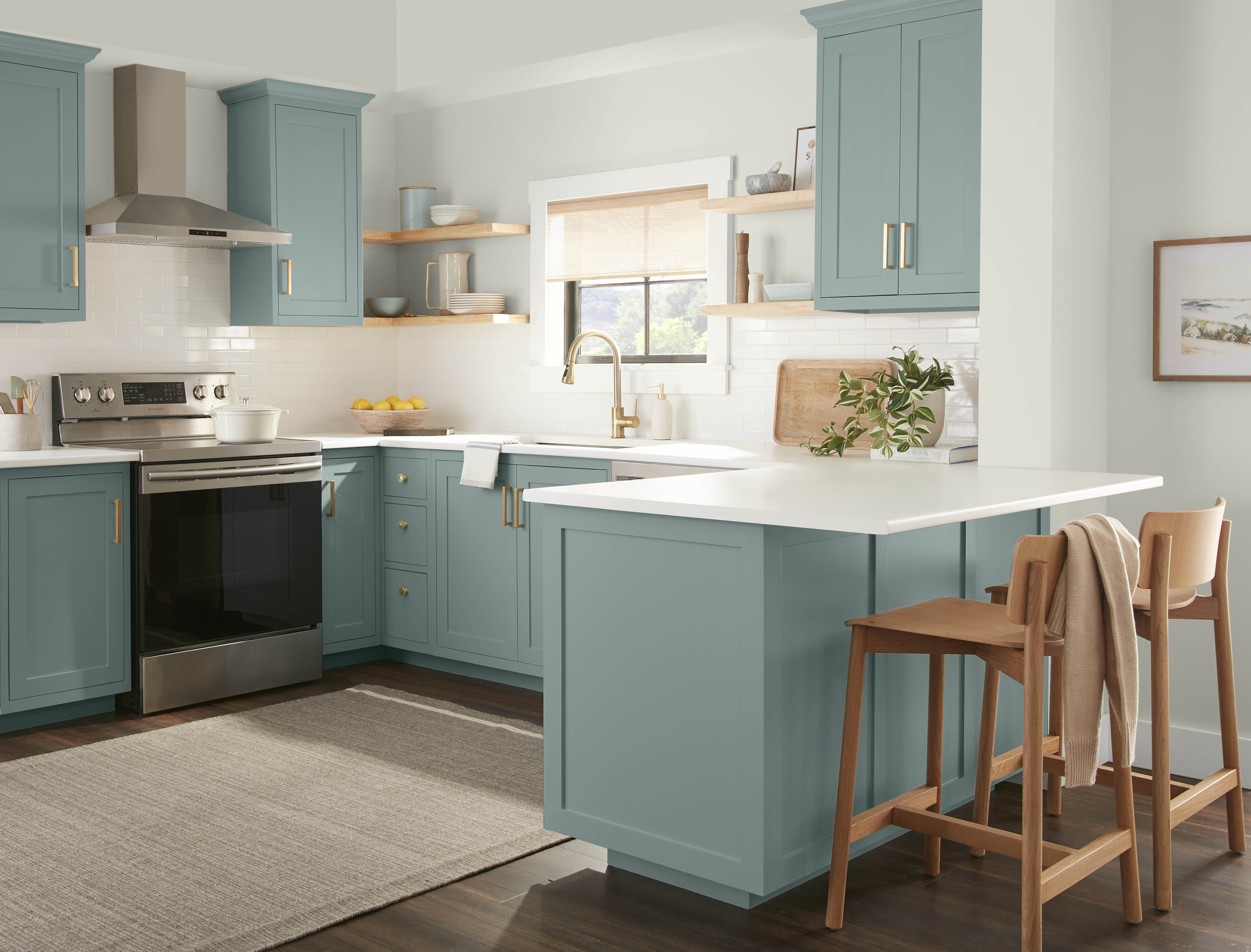 A bright white kitchen with lower and upper cabinets painted in a dusty blue green colour