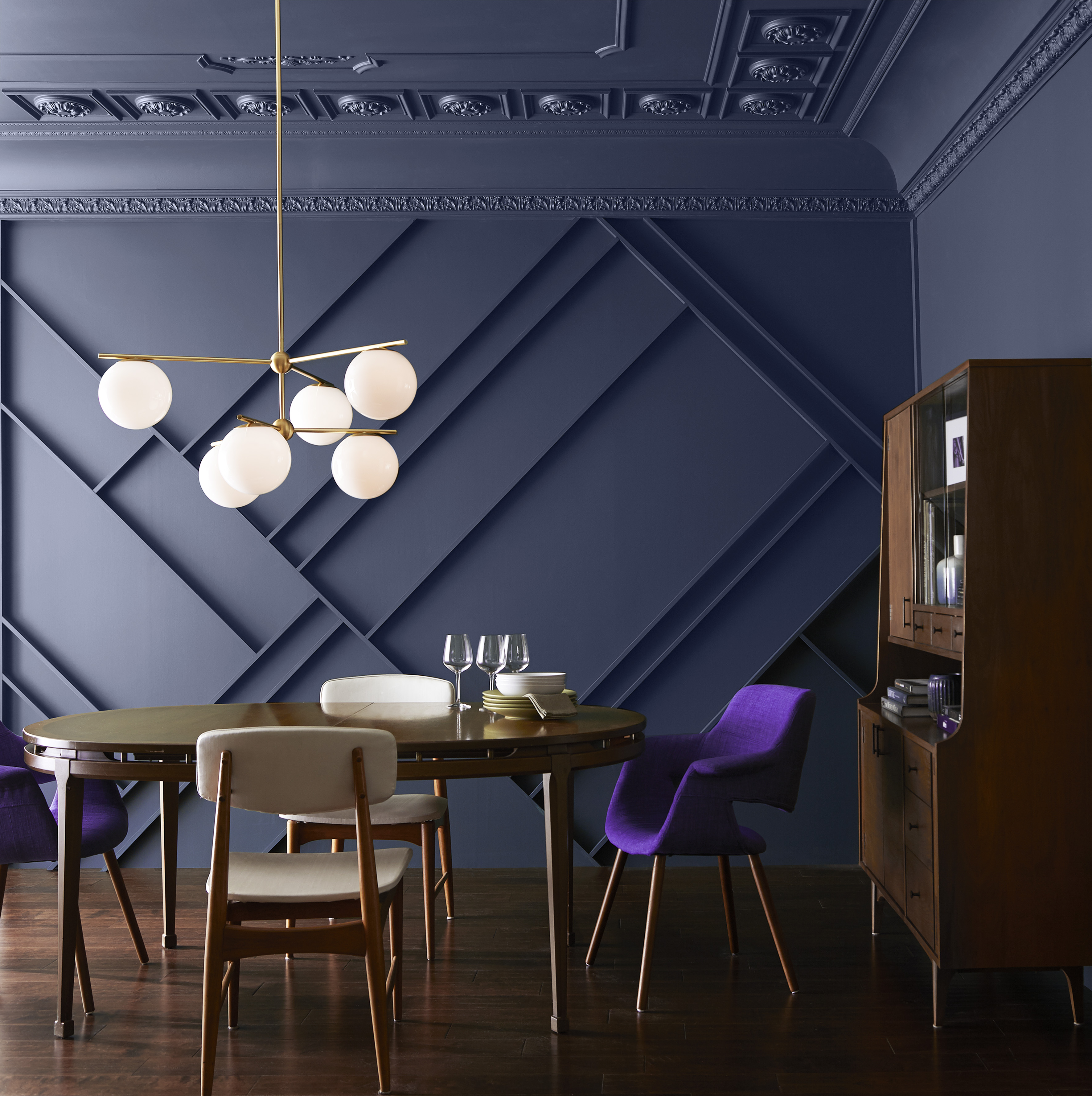 A bold dining room with walls and ceiling painted in a dark navy colour, styled with a wood dining table and chairs set and a wood cabinet 