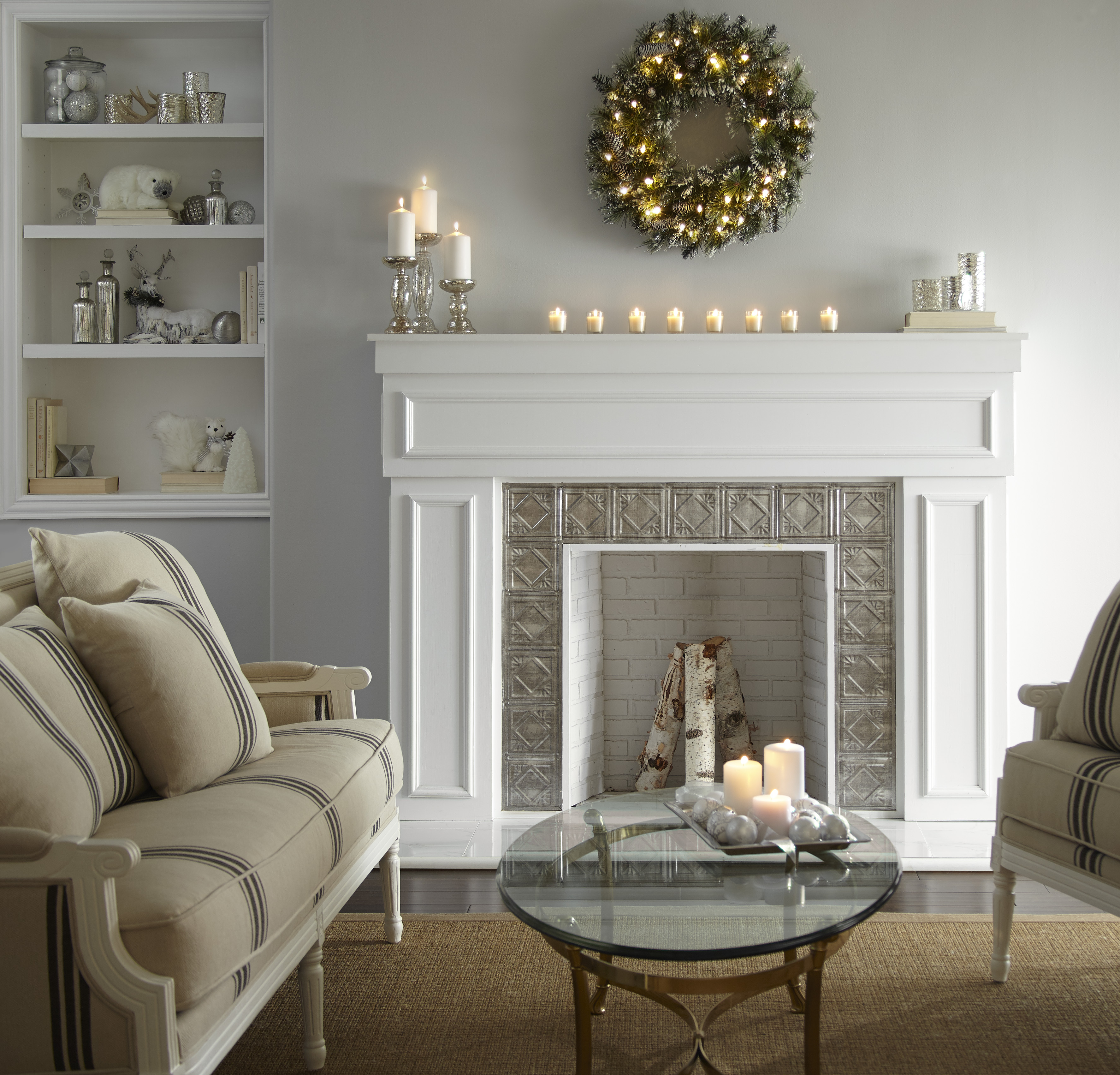A white living room with a white fireplace, styled with a holiday wreath and candles on the mantle 