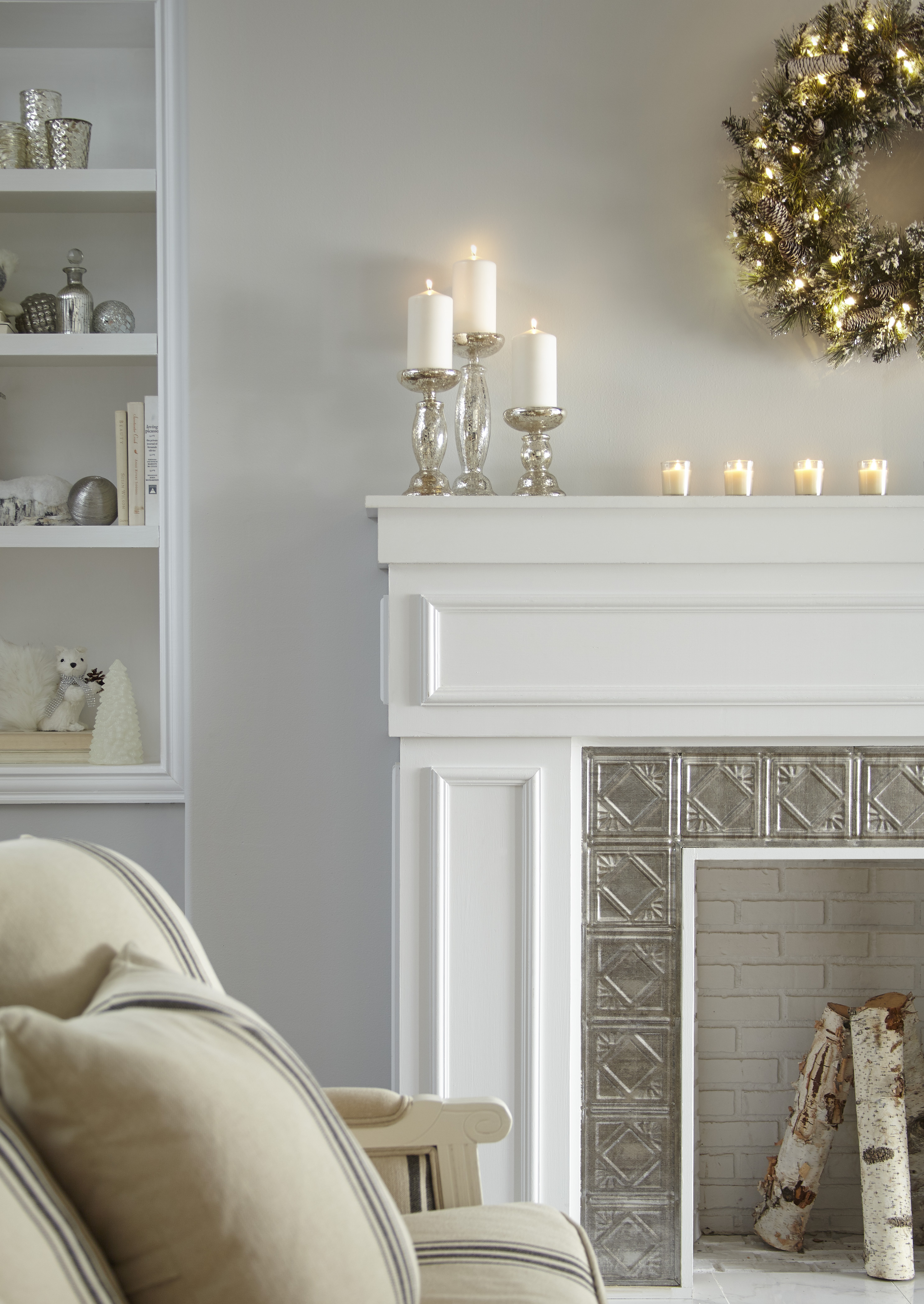 A white living room with a white fireplace, styled with a holiday wreath and candles on the mantle 
