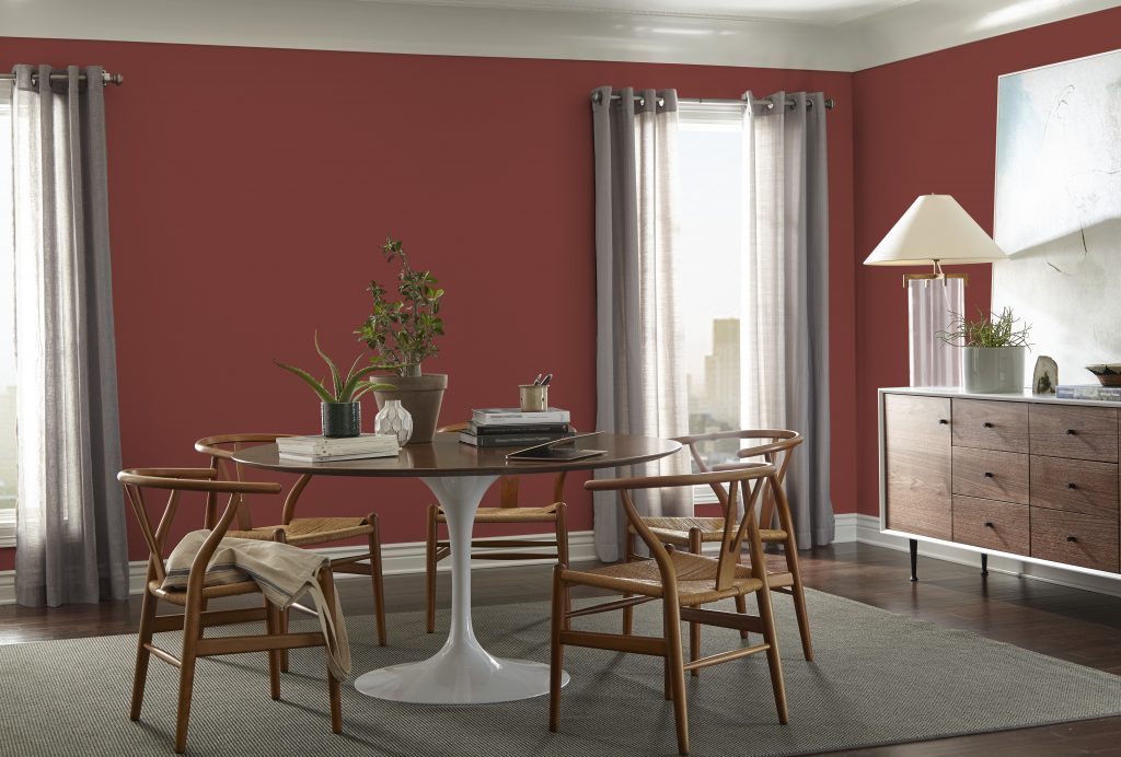 A dining room with walls painted in a bold red colour, styled with a mid-century modern dining set and sideboard