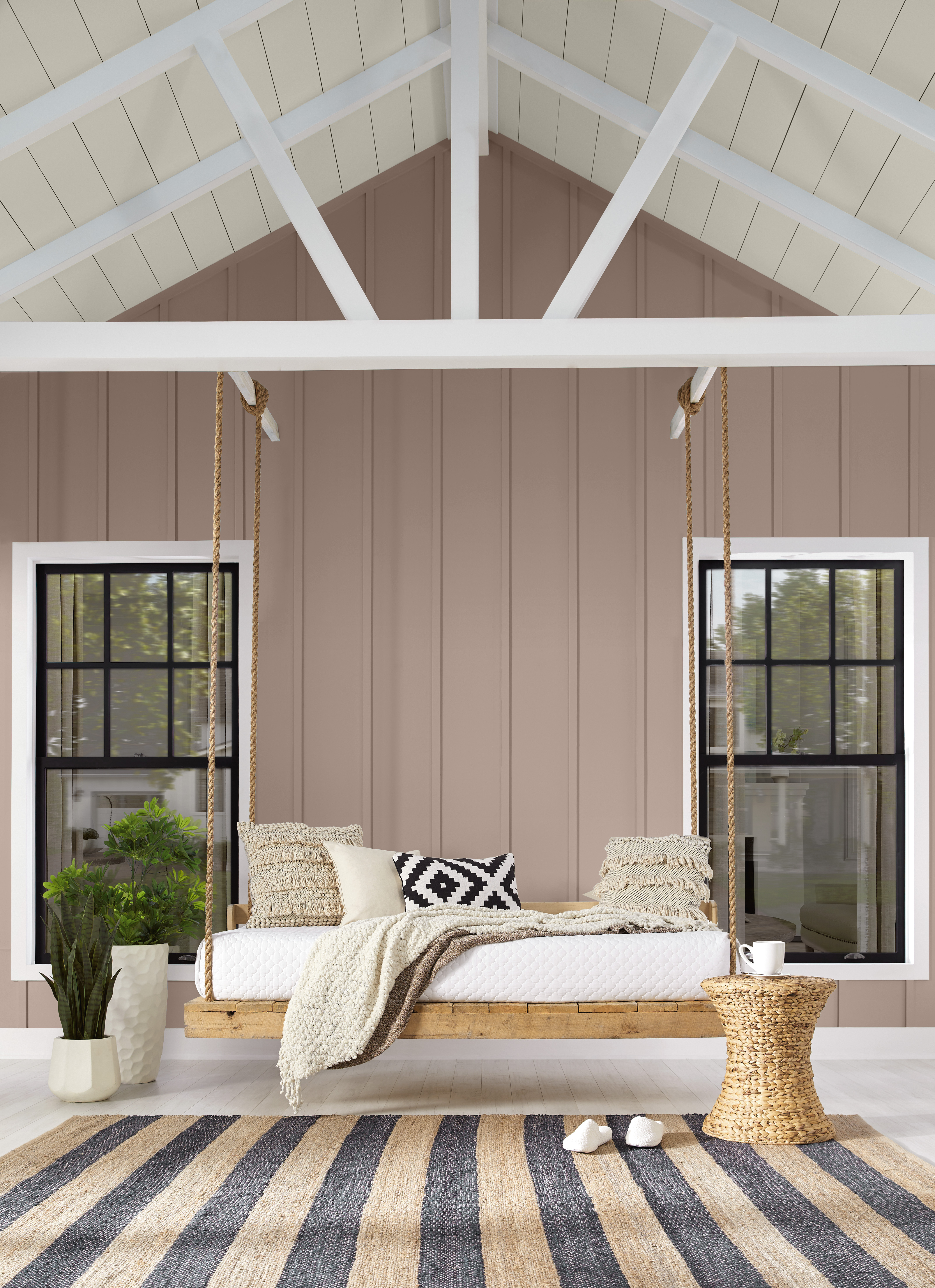 A front porch with walls painted in a taupe-mauve colour, styled with a hanging swing and striped rug