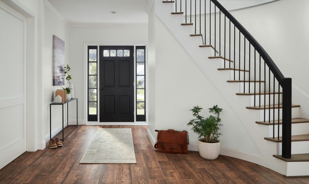 An open and airy foyer with walls painted in white, with a black door and staircase railings 