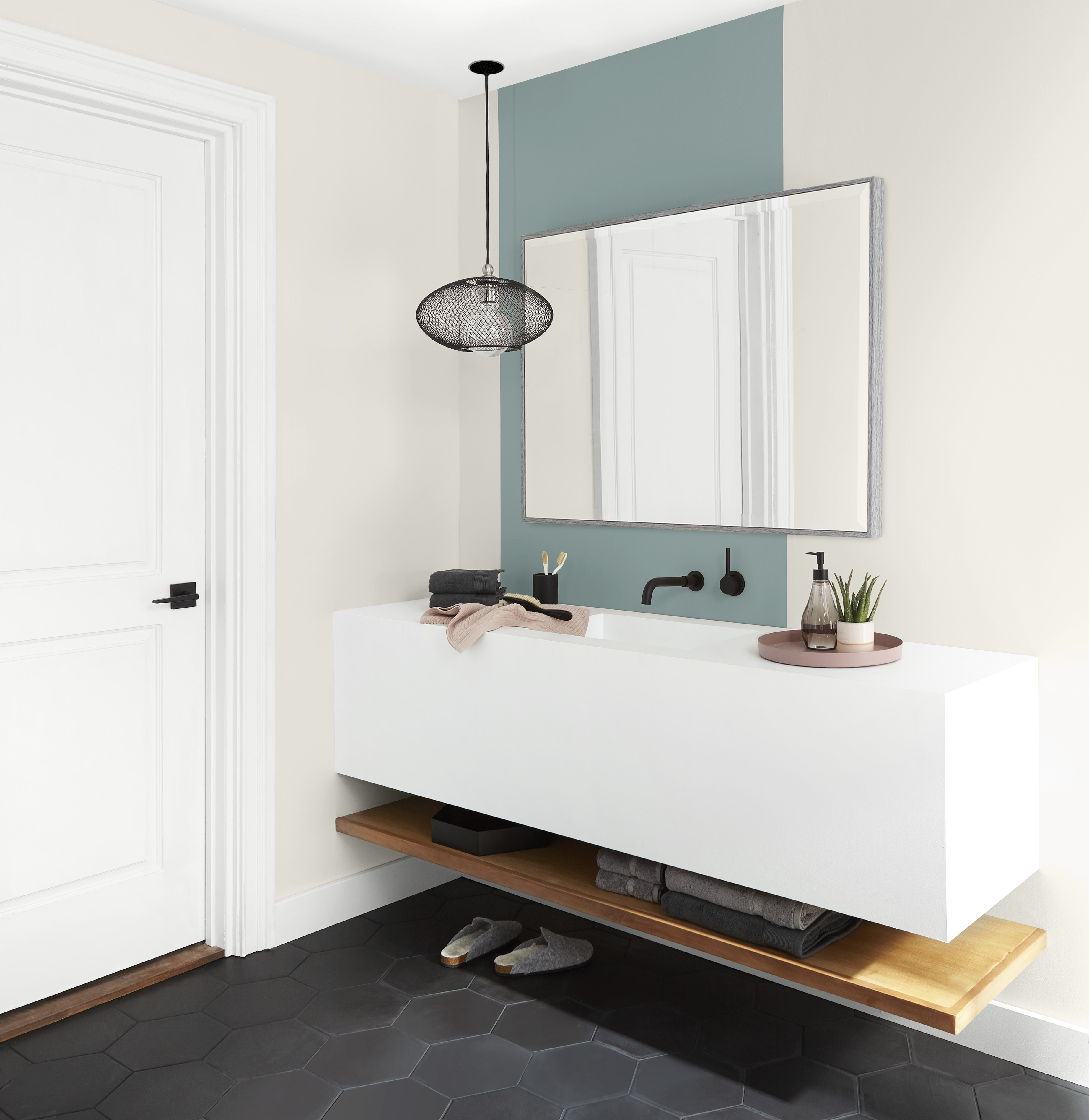 A modern bathroom with a floating sink, with an accent wall painted in a dusty mid-blue-green colour