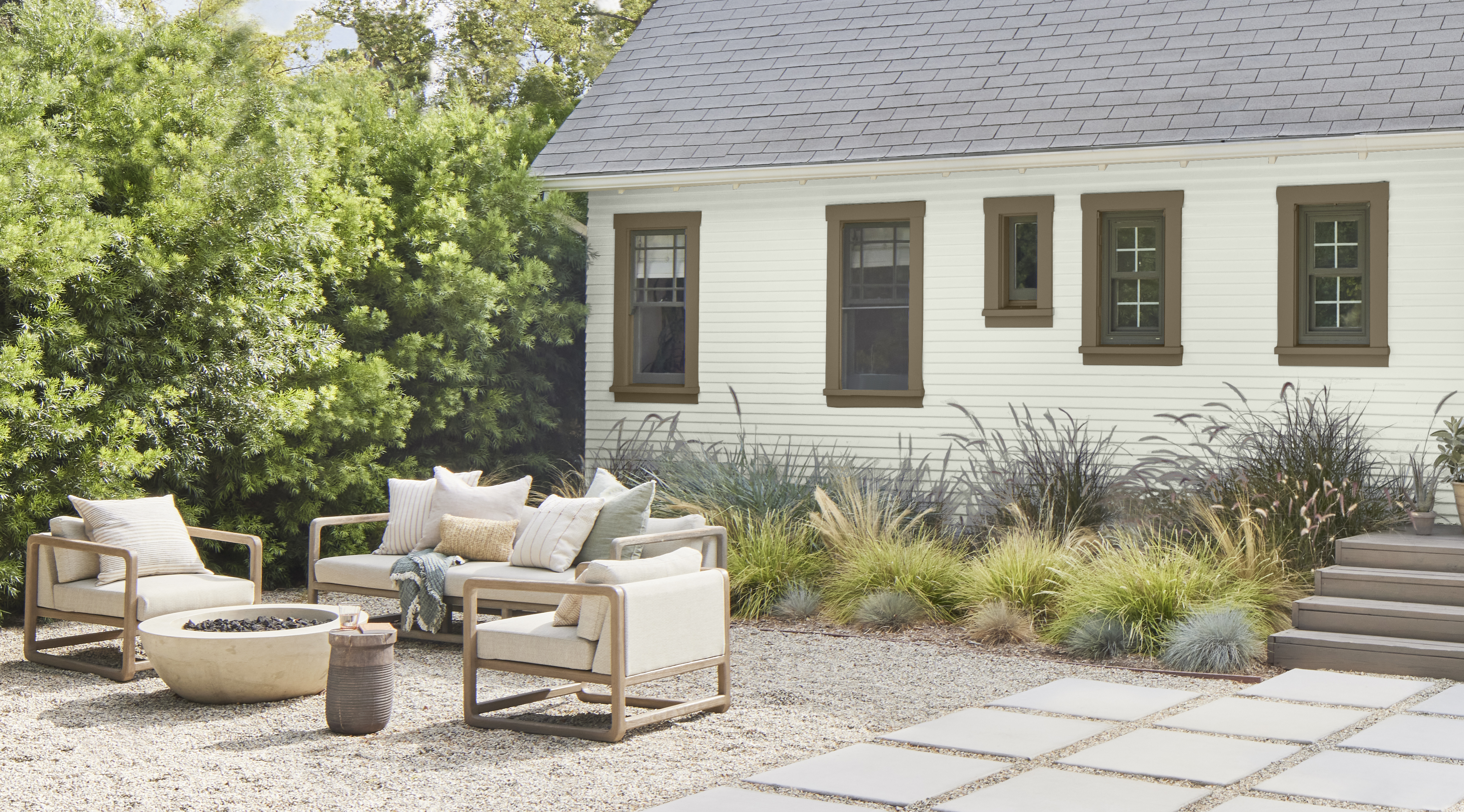 The exterior of a house with the walls painted in a cool wintery white colour, with a backyard firepit and outdoor seating area