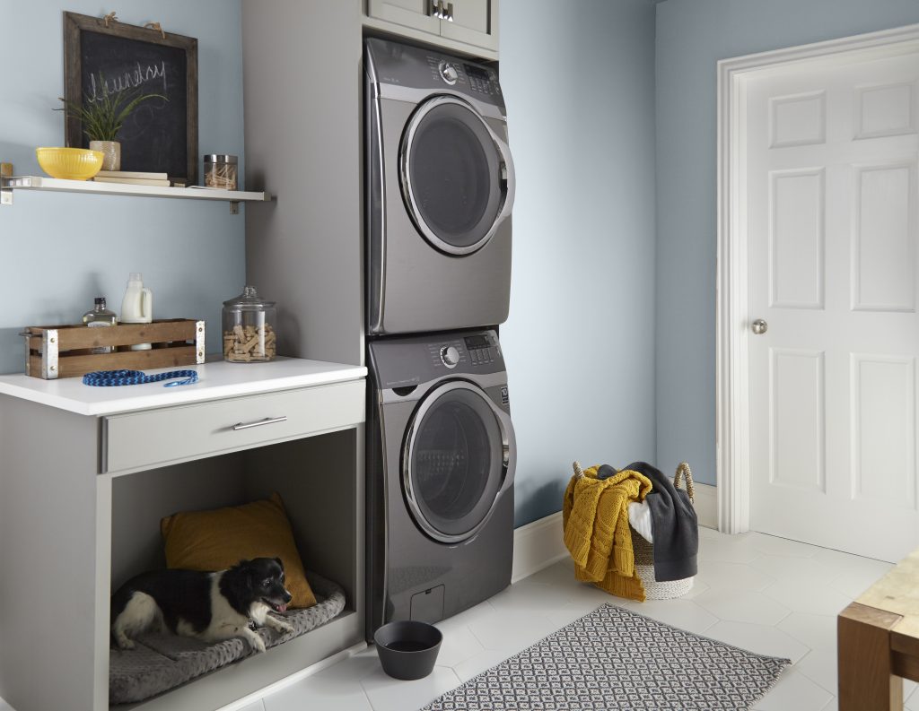 A spacious laundry room with walls painted in a light blue-grey colour, with a stacked washer and dryer