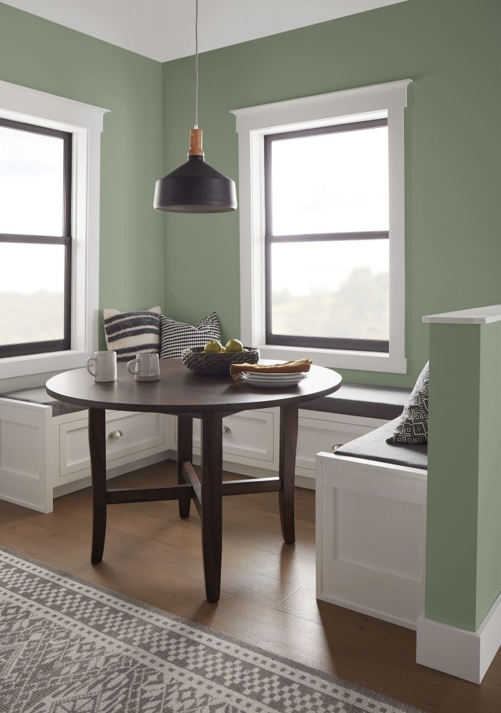 A cozy dining nook with walls painted in a muted green colour and white and black trim