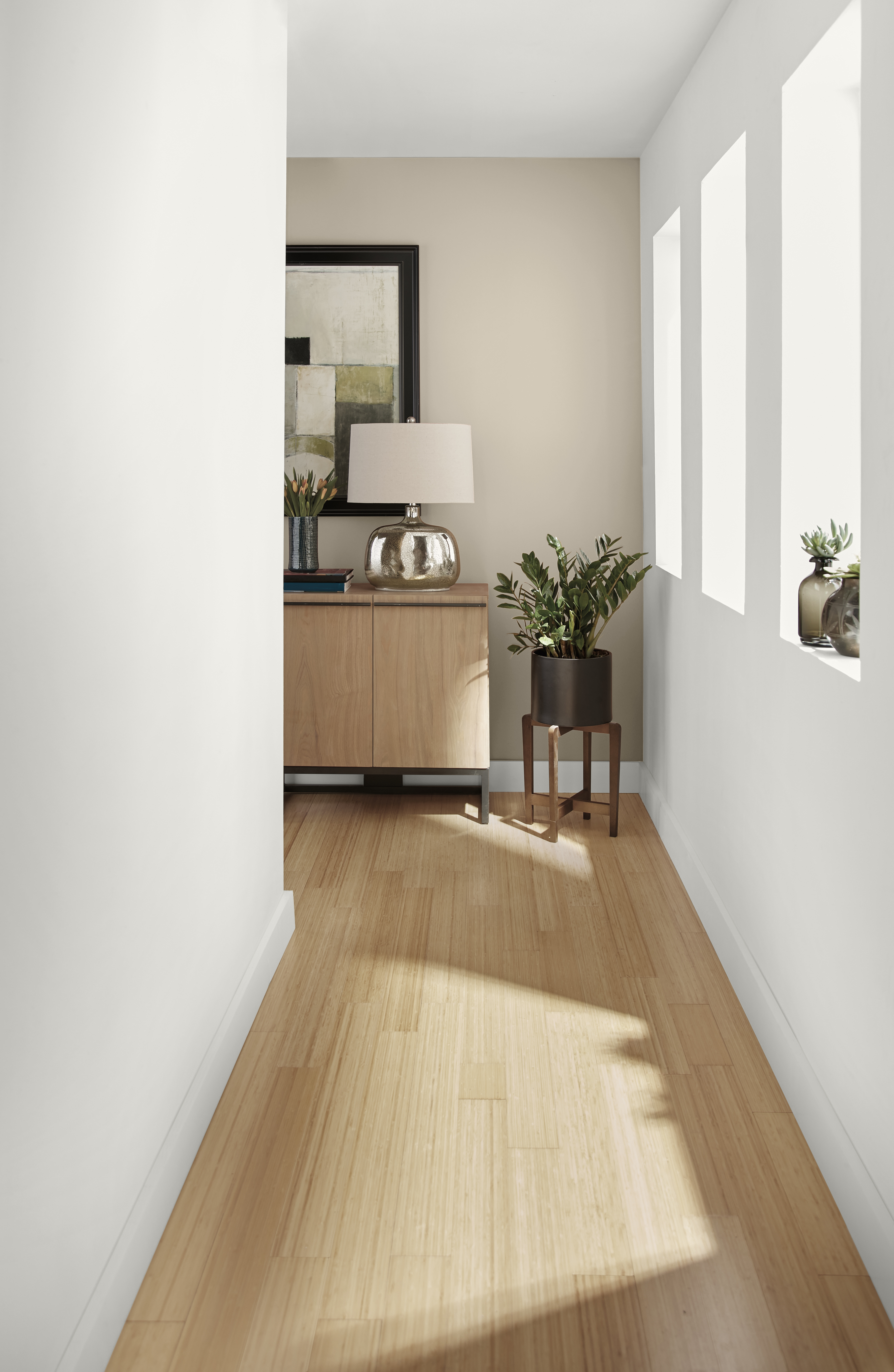 A long hallway with walls painted in white, leading to a partial view of a modern living room