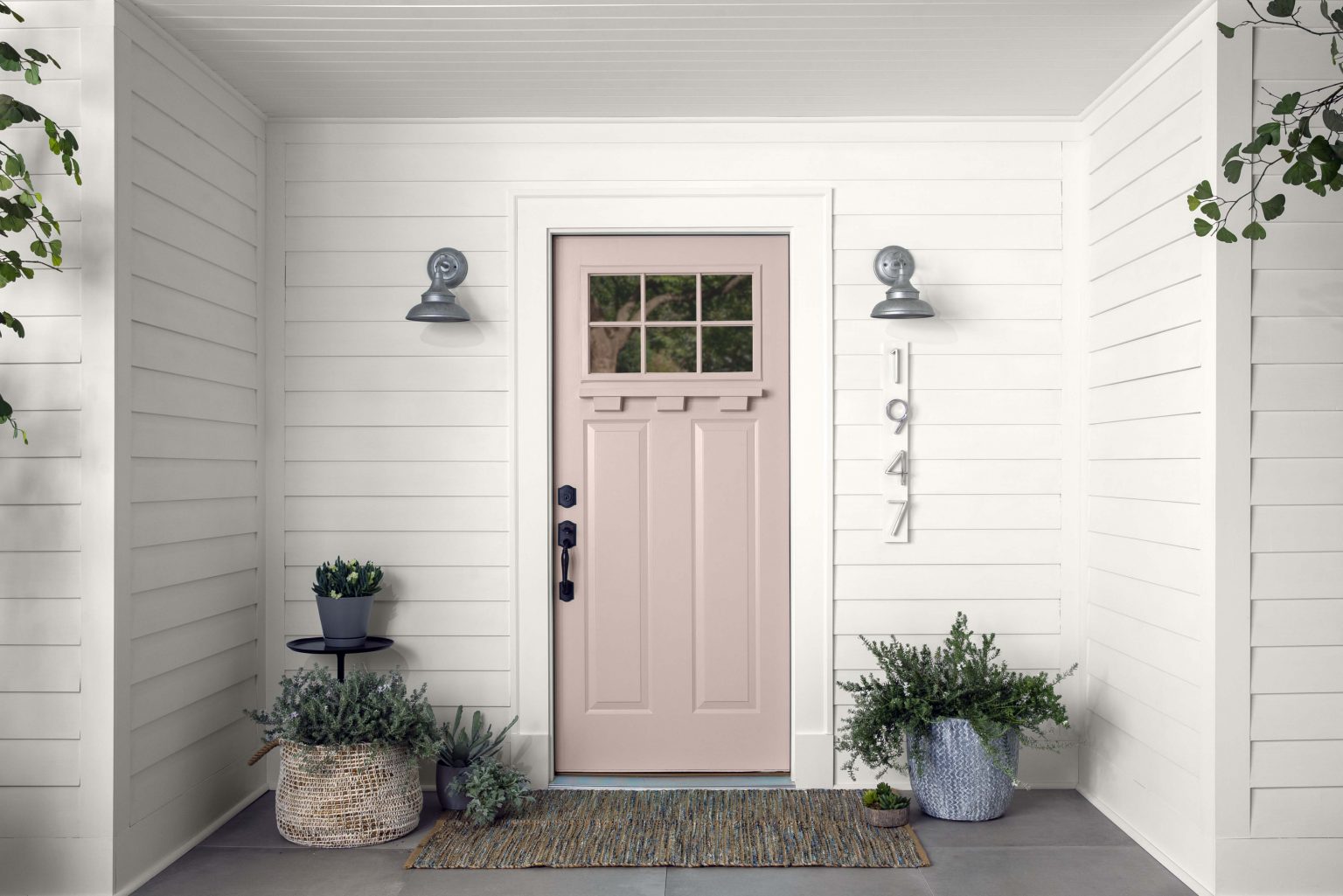 A closeup of an exterior porch, with walls painted in white and the front door painted in a neutral light pink colour