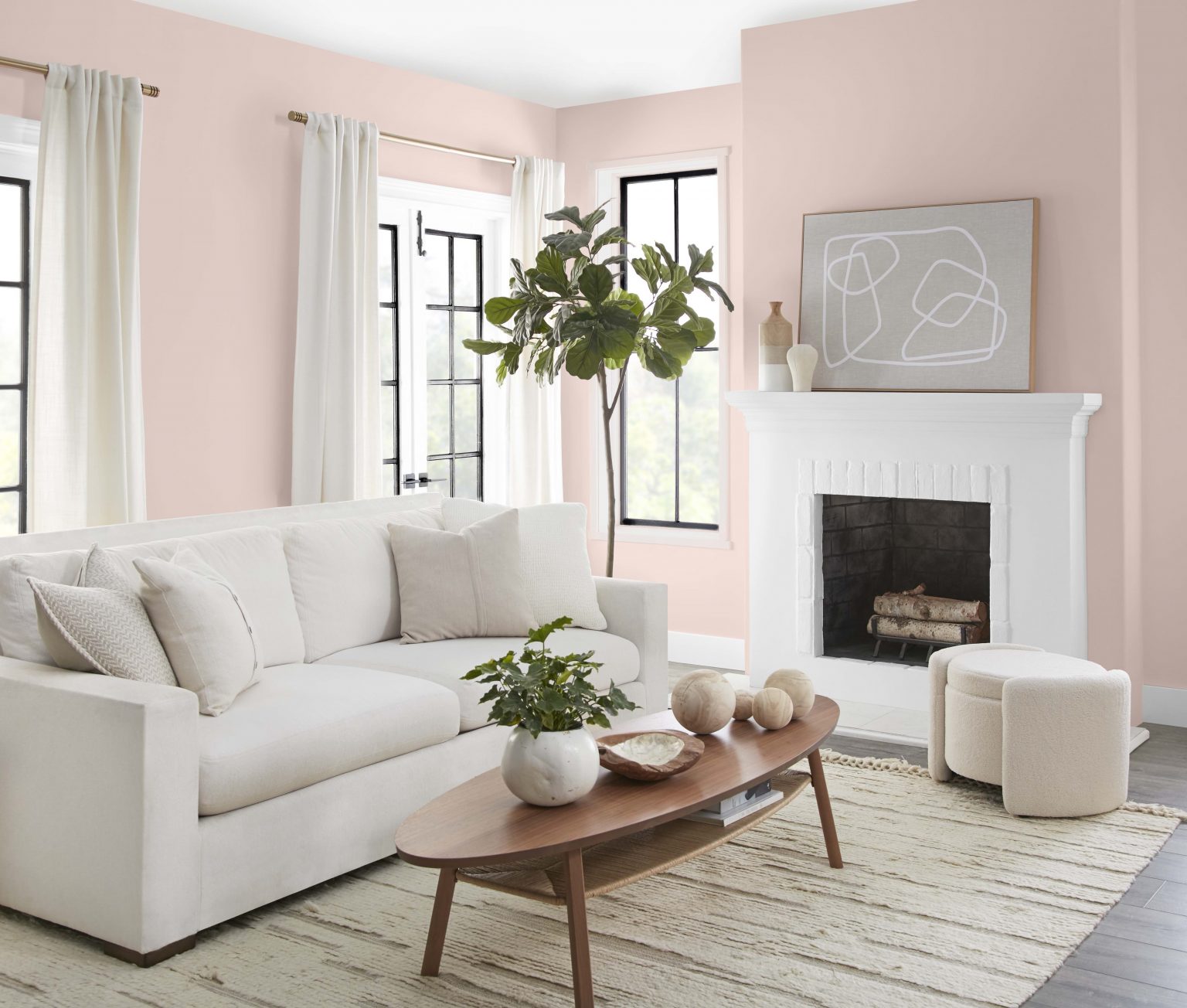 A casual living room with walls painted in a neutral light pink colour, with a white fireplace mantle, black and white window trim, and neutral furniture 