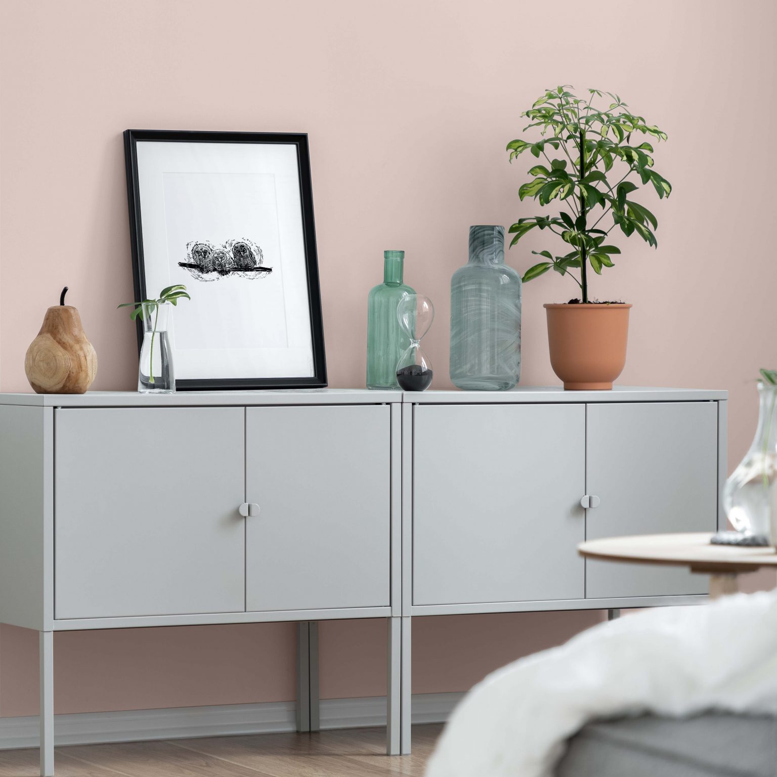 A closeup of a room with walls painted in a neutral light pink colour, styled with a simple grey sideboard and a variety of décor pieces