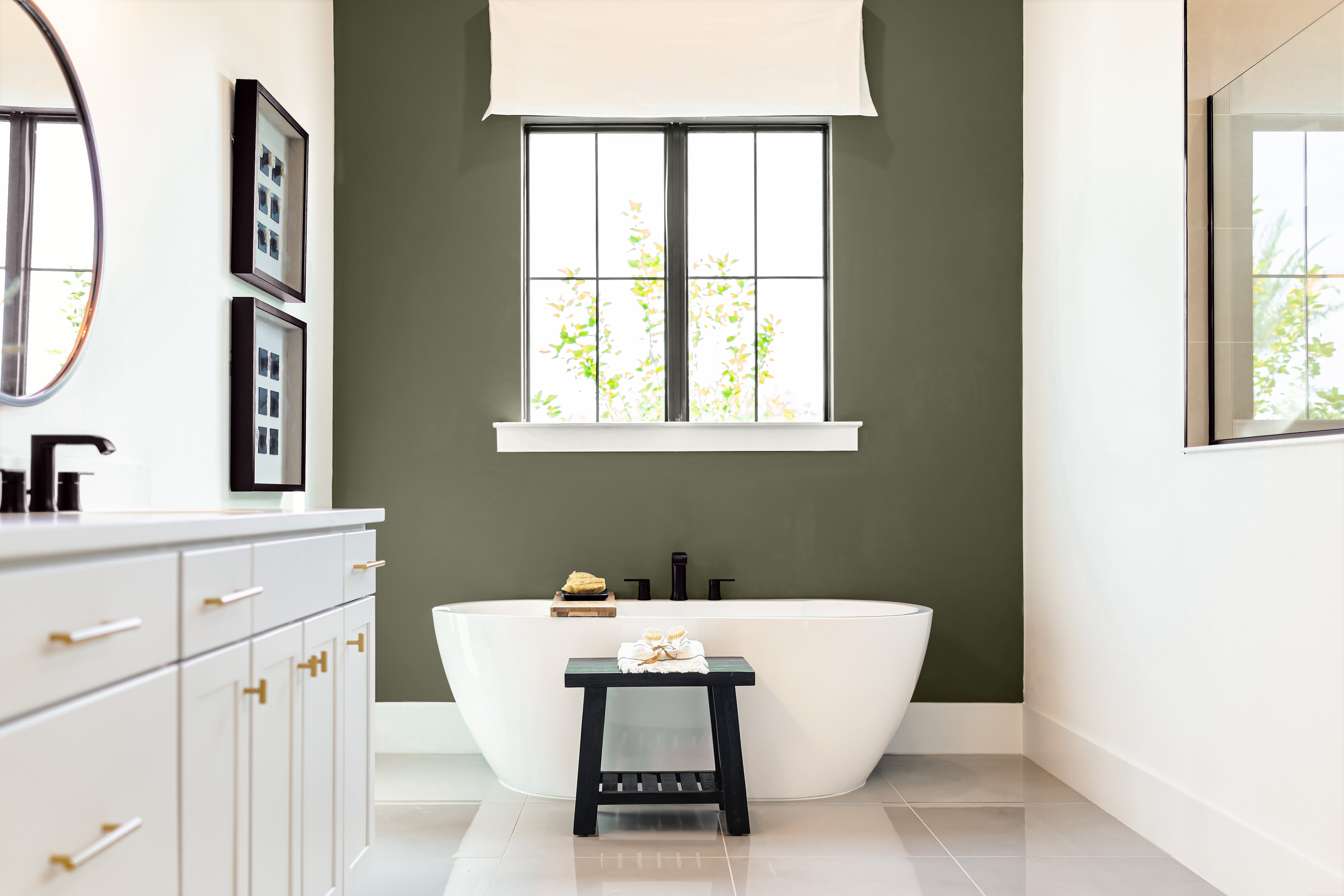 A large bathroom with two walls painted in white and an accent wall in the middle painted in a dark olive green colour, with a free standing bathtub 