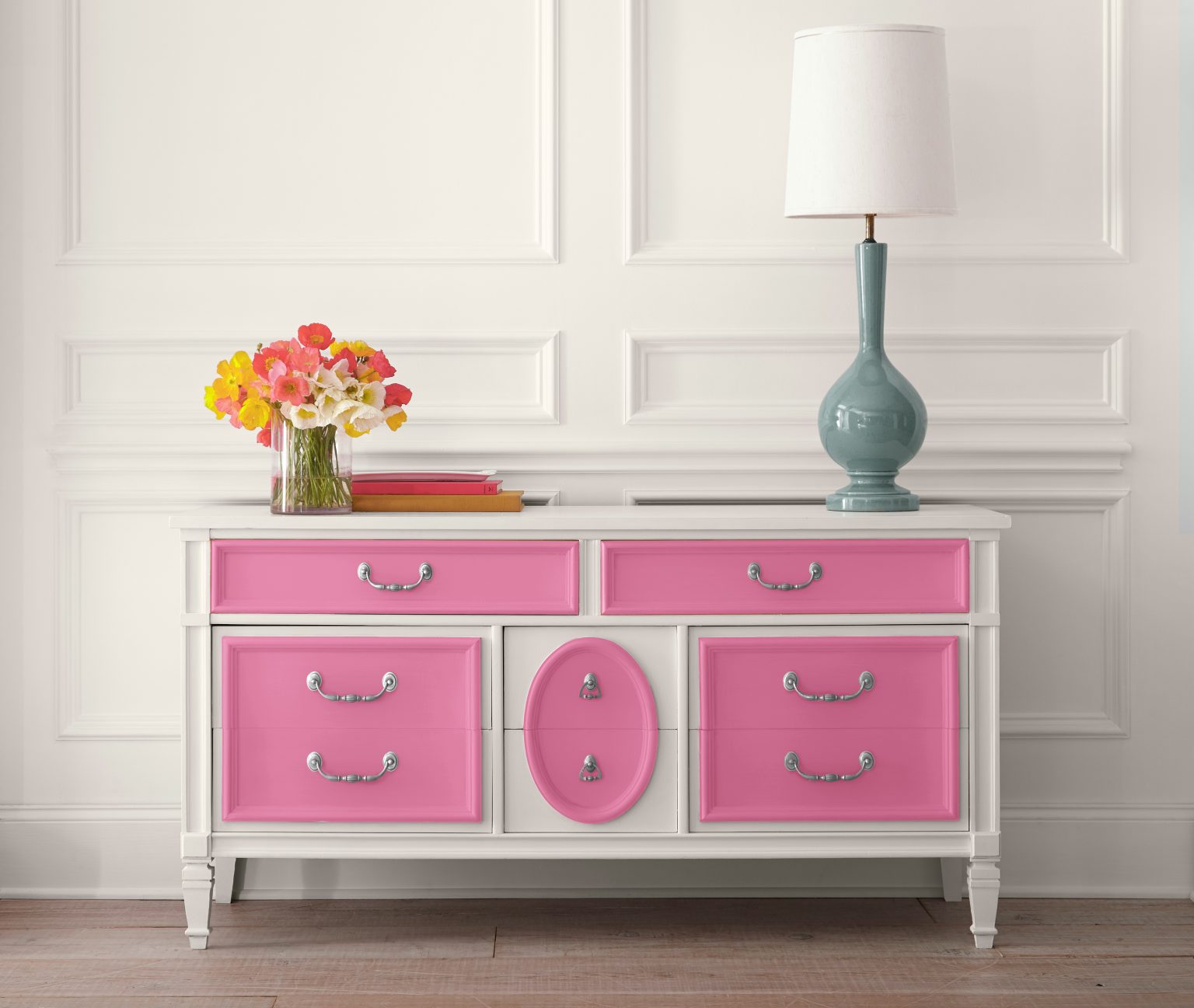 A closeup of a white dresser with doors painted in a bright pink colour and silver handles