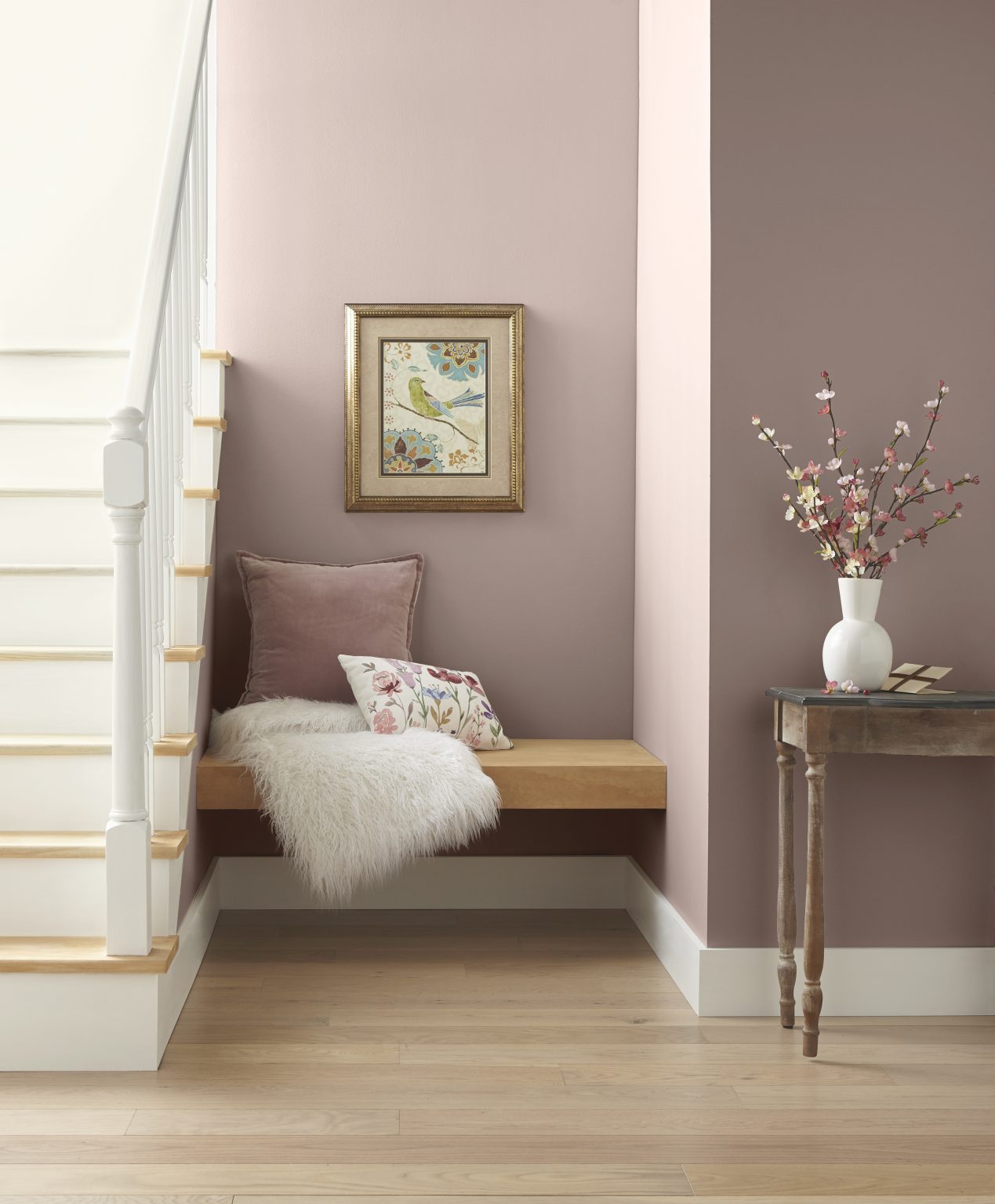 A small nook near the stairs with walls painted in a dusty pink colour, styled with neutral furniture and décor