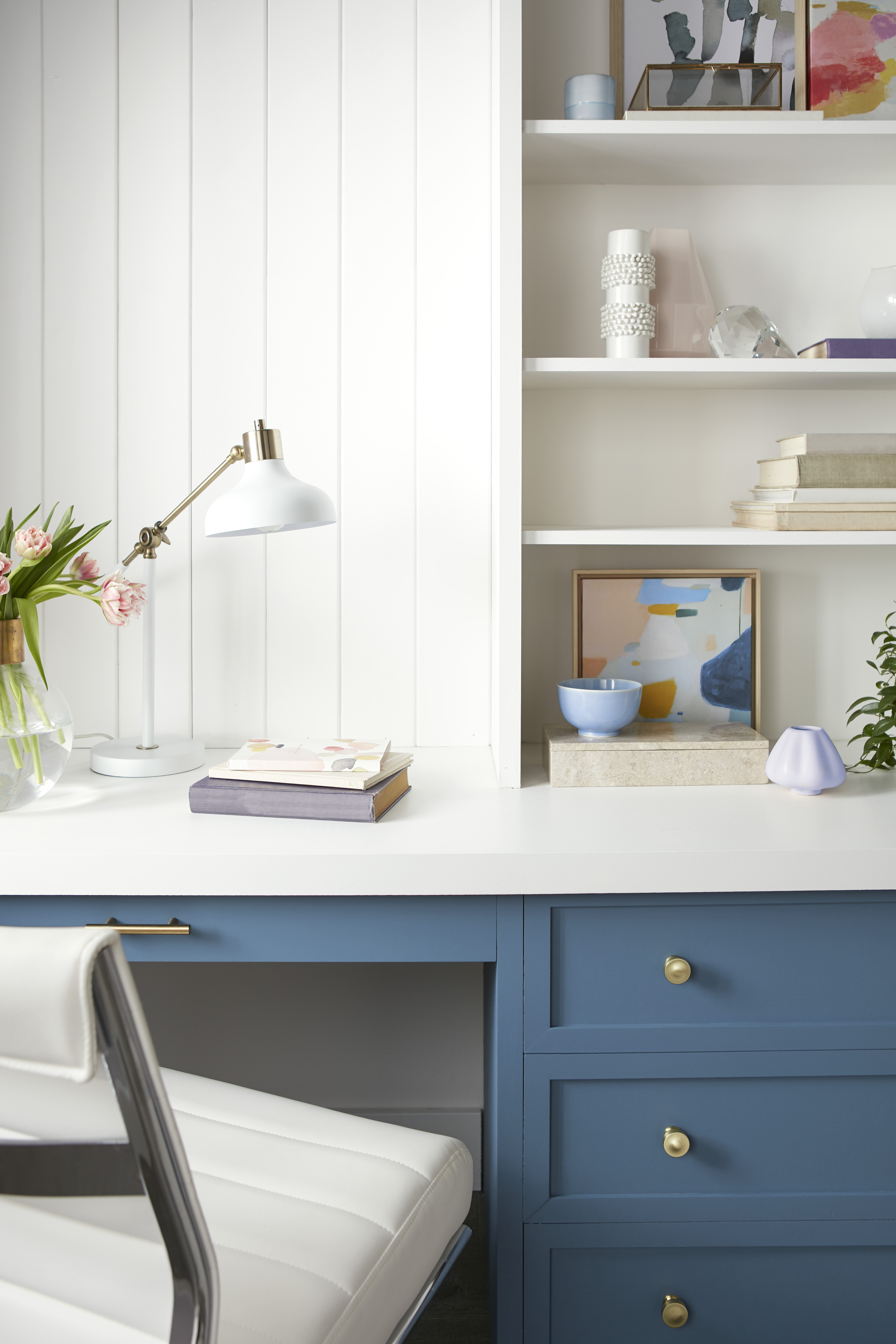 A closeup of a built-in desk painted in blue, with walls and shelving painted in white