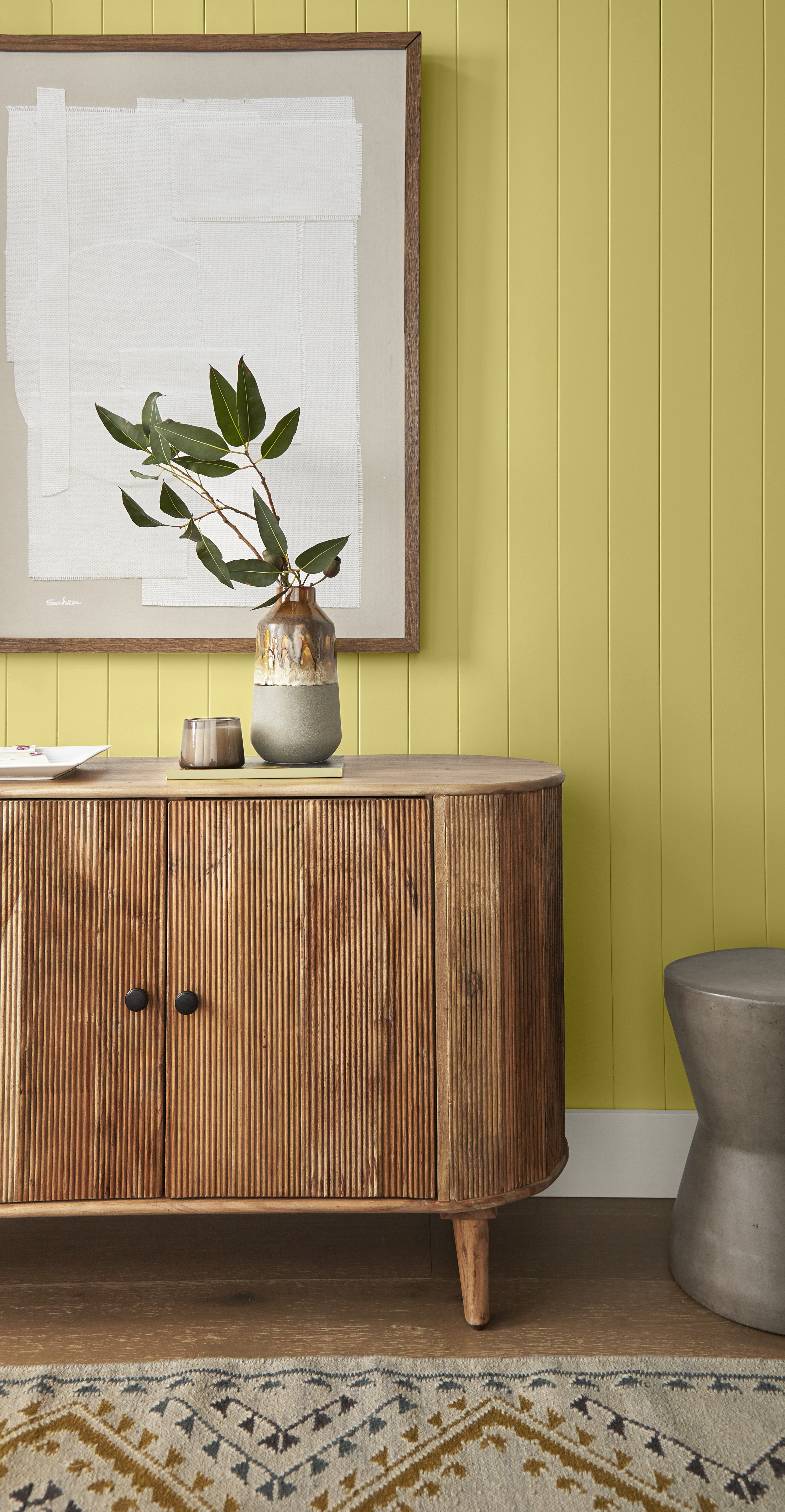 A closeup of a wood console, with the paneled walls behind it painted in a greenish-yellow colour