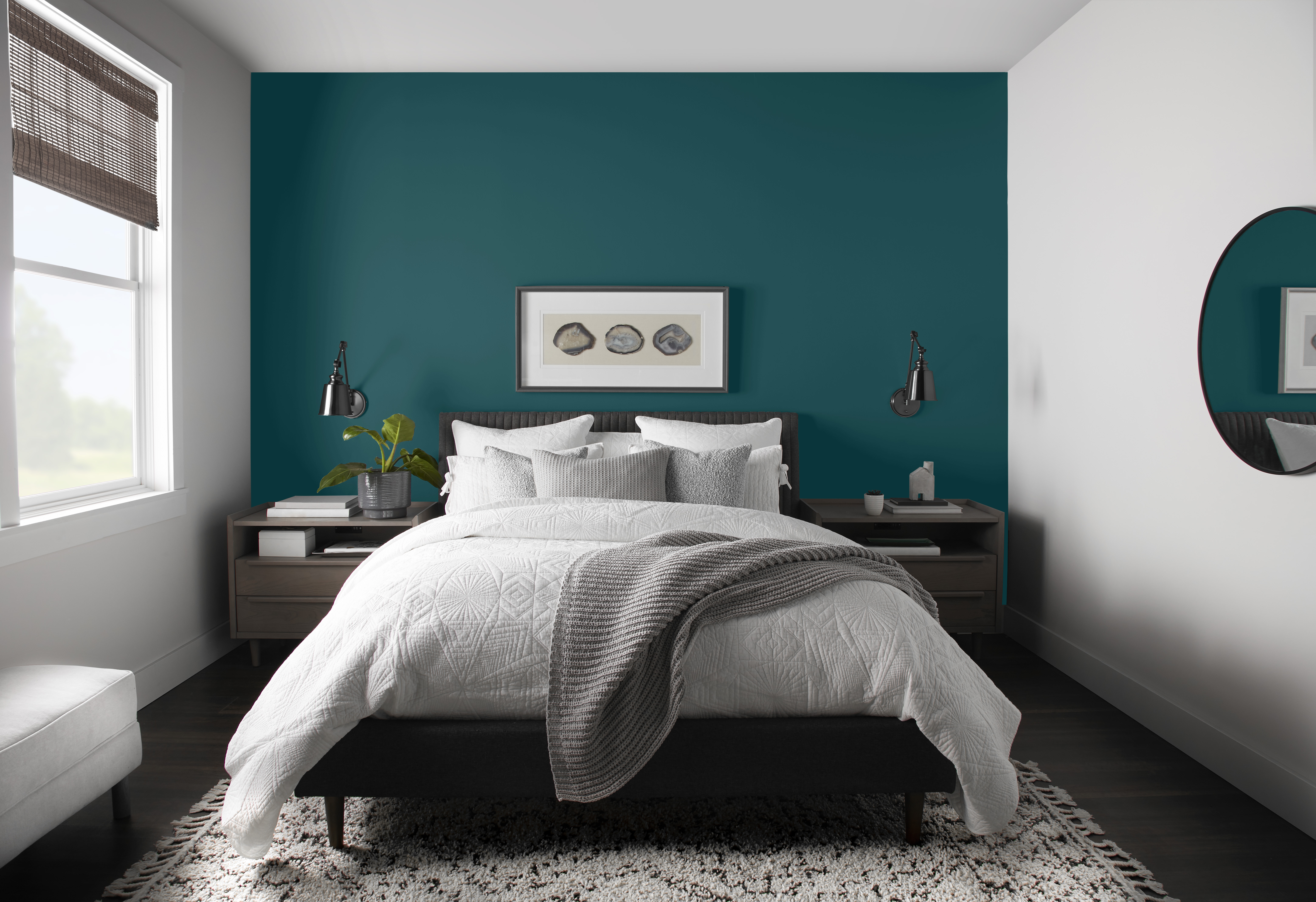A white bedroom with the bed headboard accent wall painted in a deep teal colour 