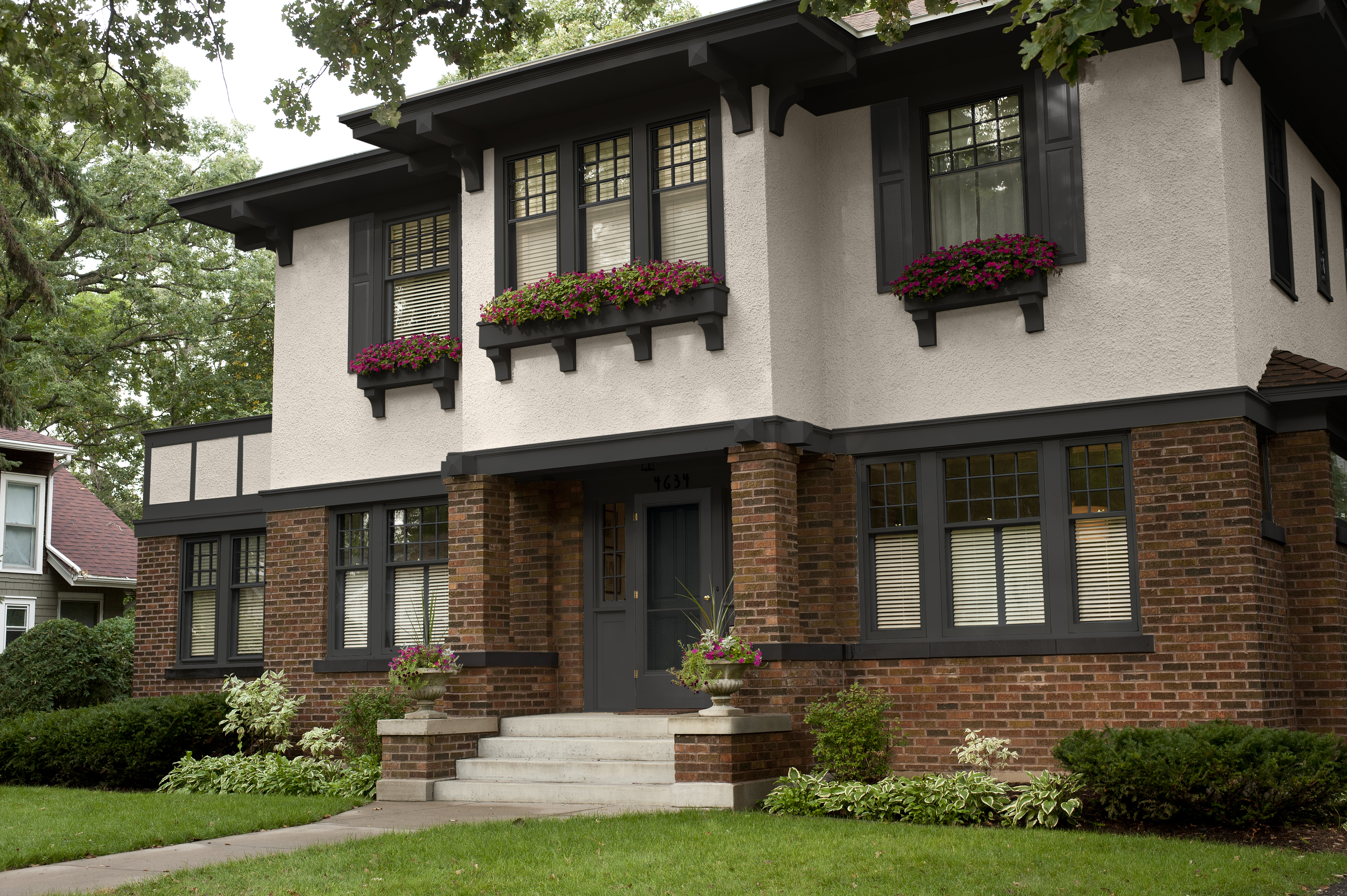 The exterior of a two-story house with beige stucco, red and brown brick, and black trim and accents