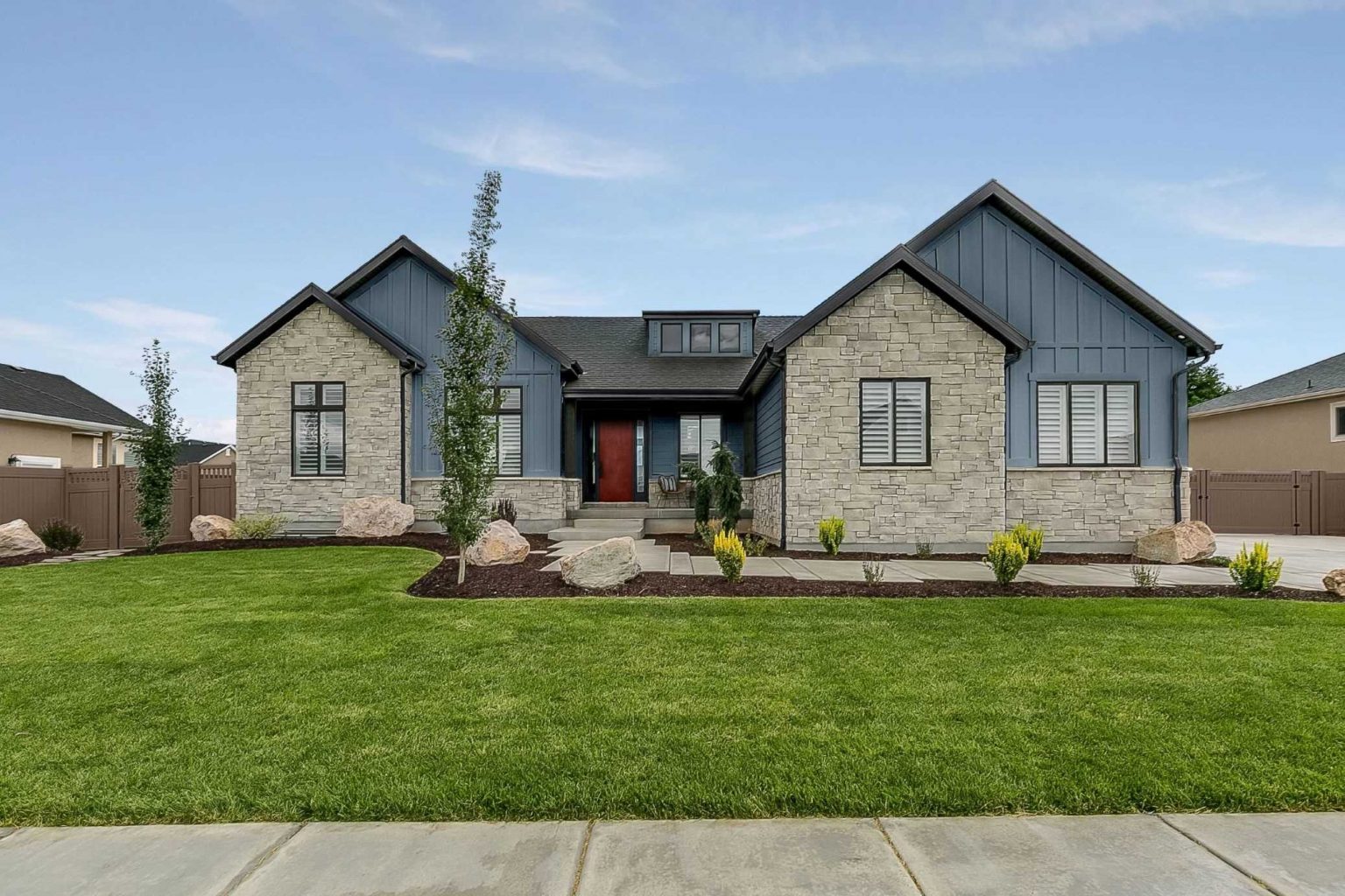 The exterior of a modern farmhouse home with siding painted in a dark blue colour with a red door