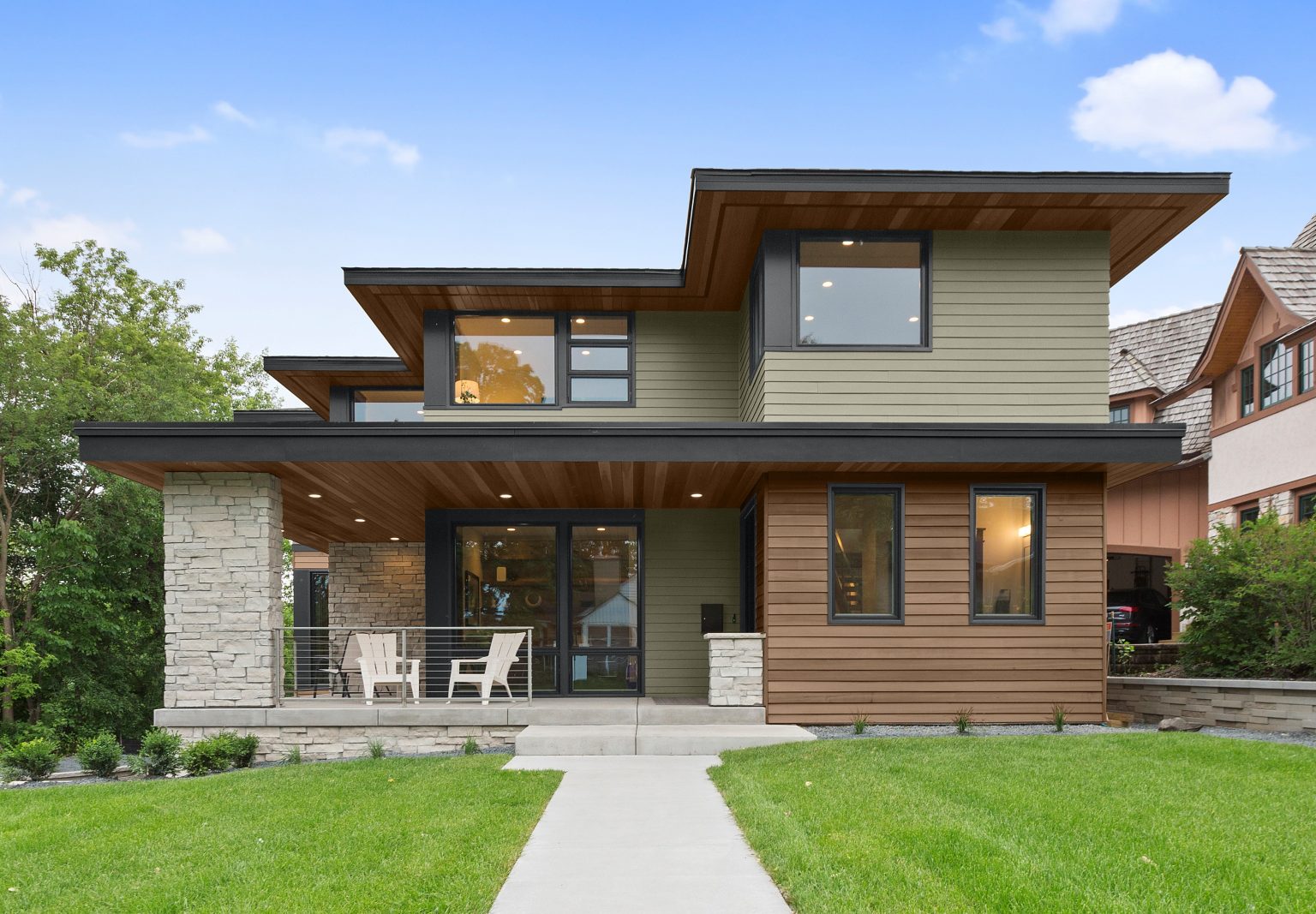 The exterior of a modern two-story house with wood accents and siding painted in an earthy green colour