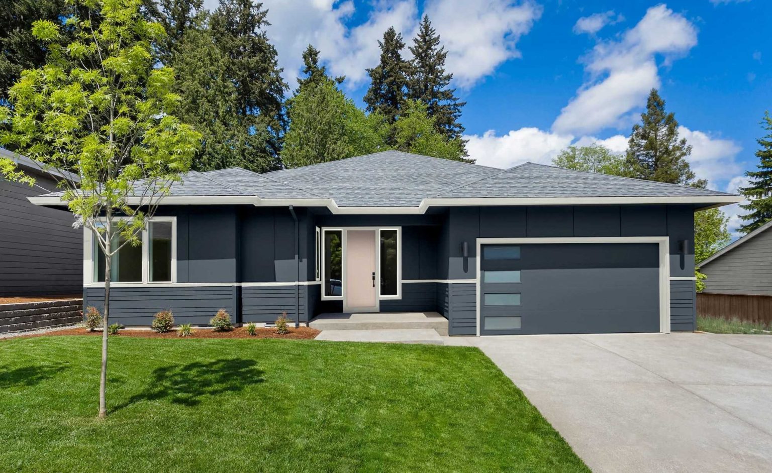 The exterior of a modern Ranch style house painted in a dark blue colour with a light pink door 