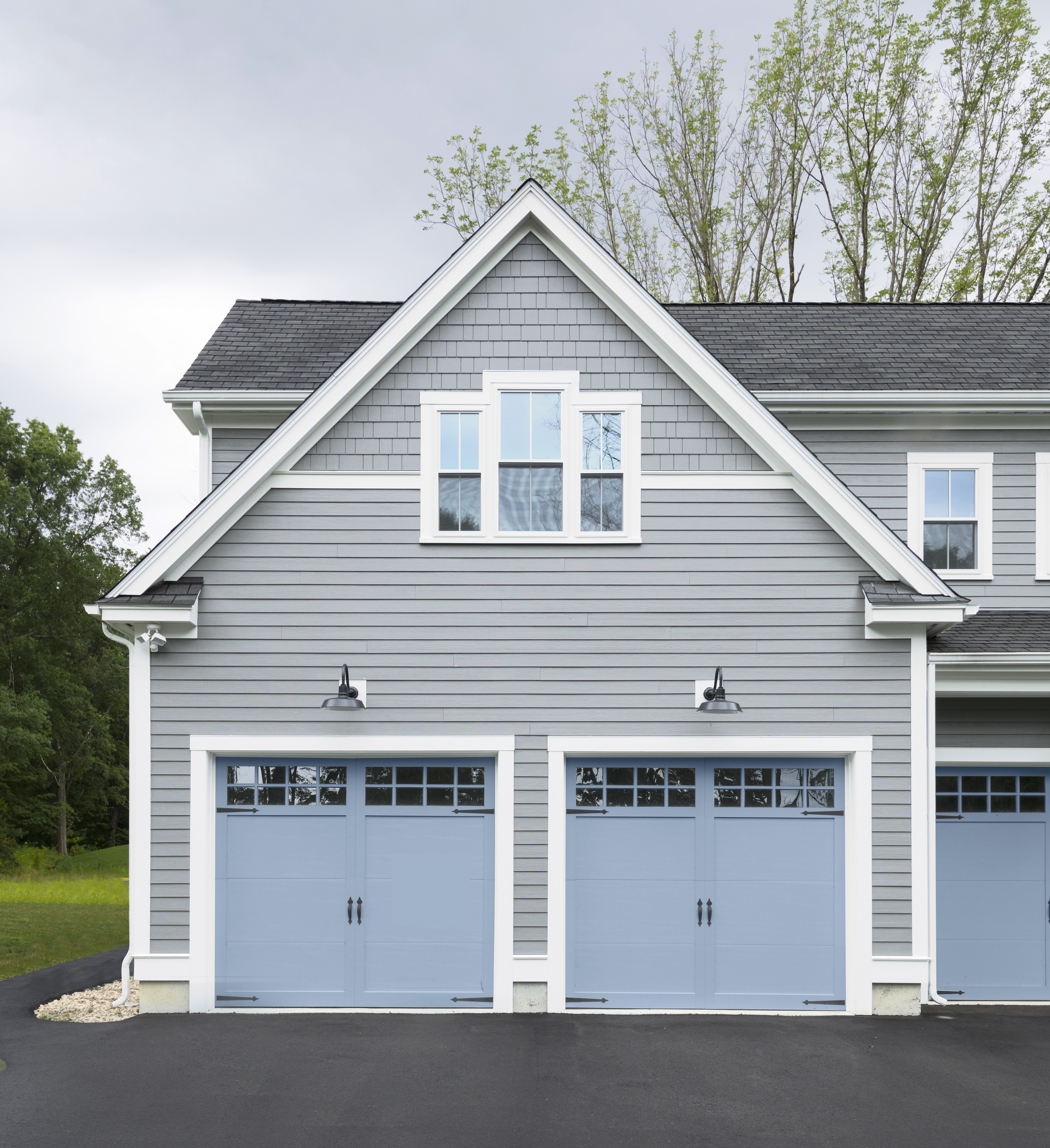 A gray-coloured home exterior with garage doors painted in an unexpected blue colour, adding a unique and refreshing touch to the overall design.