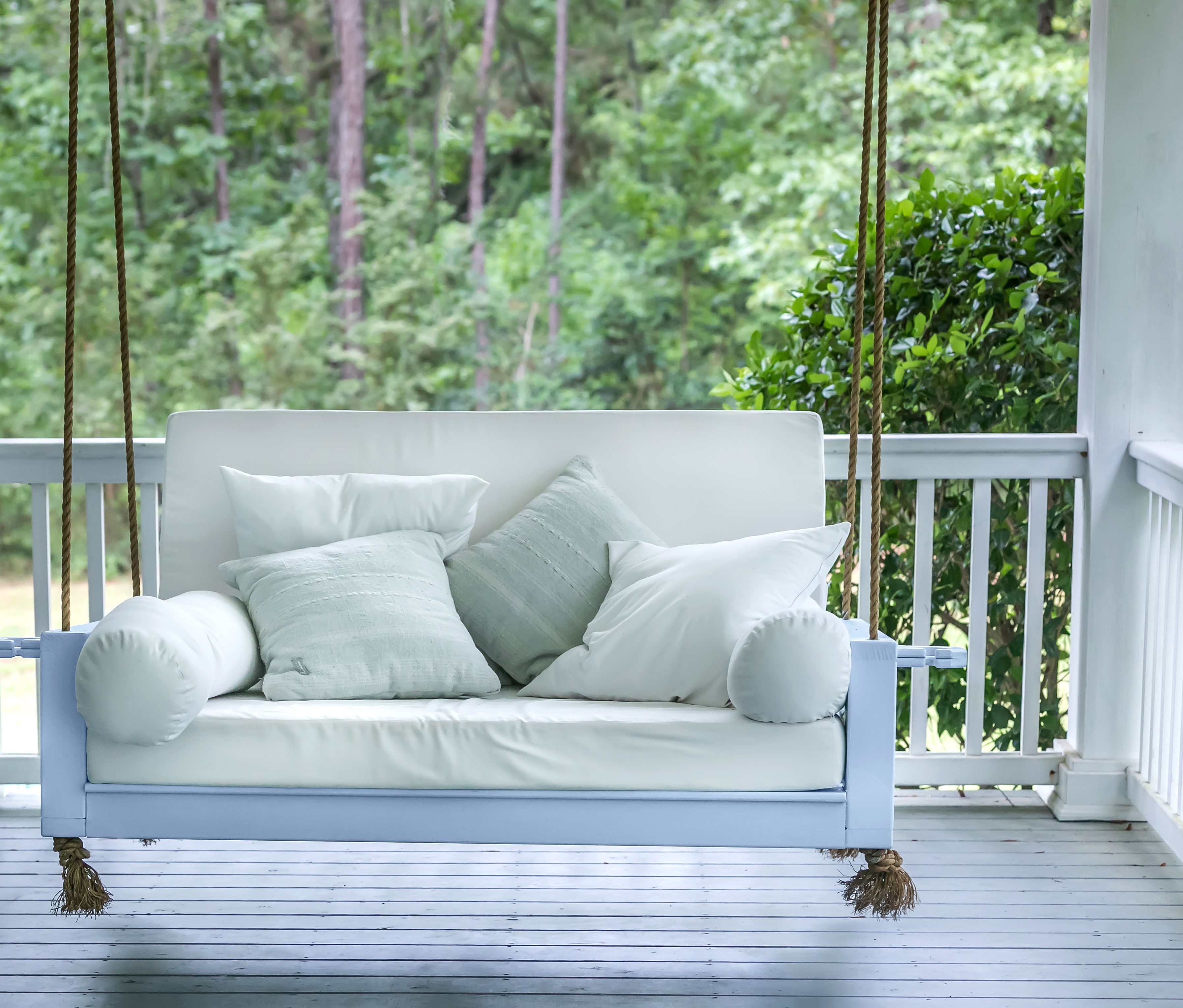 A home porch with a charming light blue swing adorned with decorative pillows, creating a welcoming and inviting space for relaxation and enjoyment.