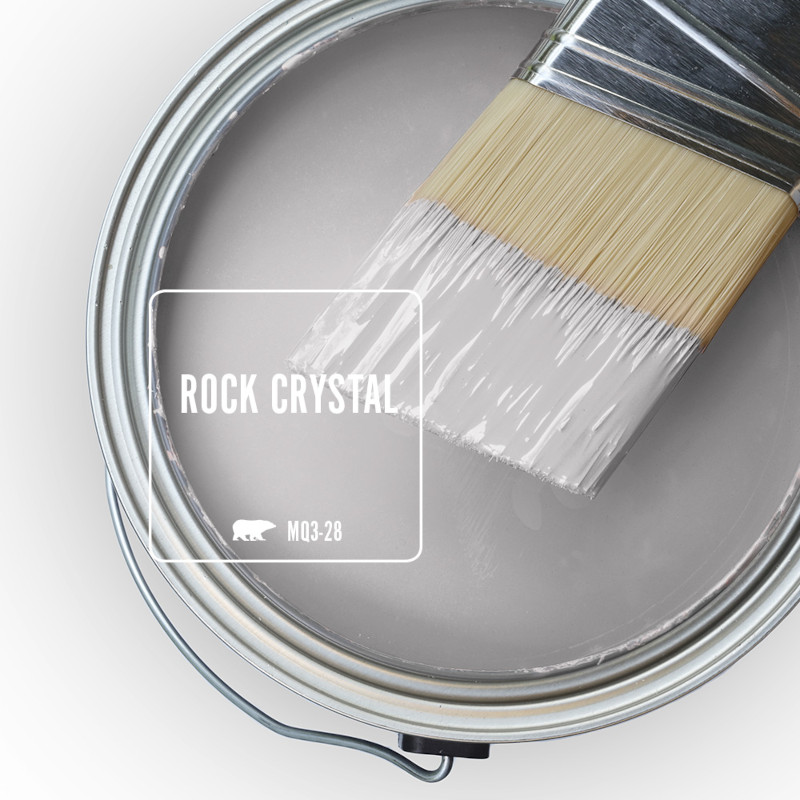 The top view of an open paint can, the paint colour is Rock Crystal, a light grey with notes of lilac. There is a half-dipped paint brush leaning on top of the can rim.