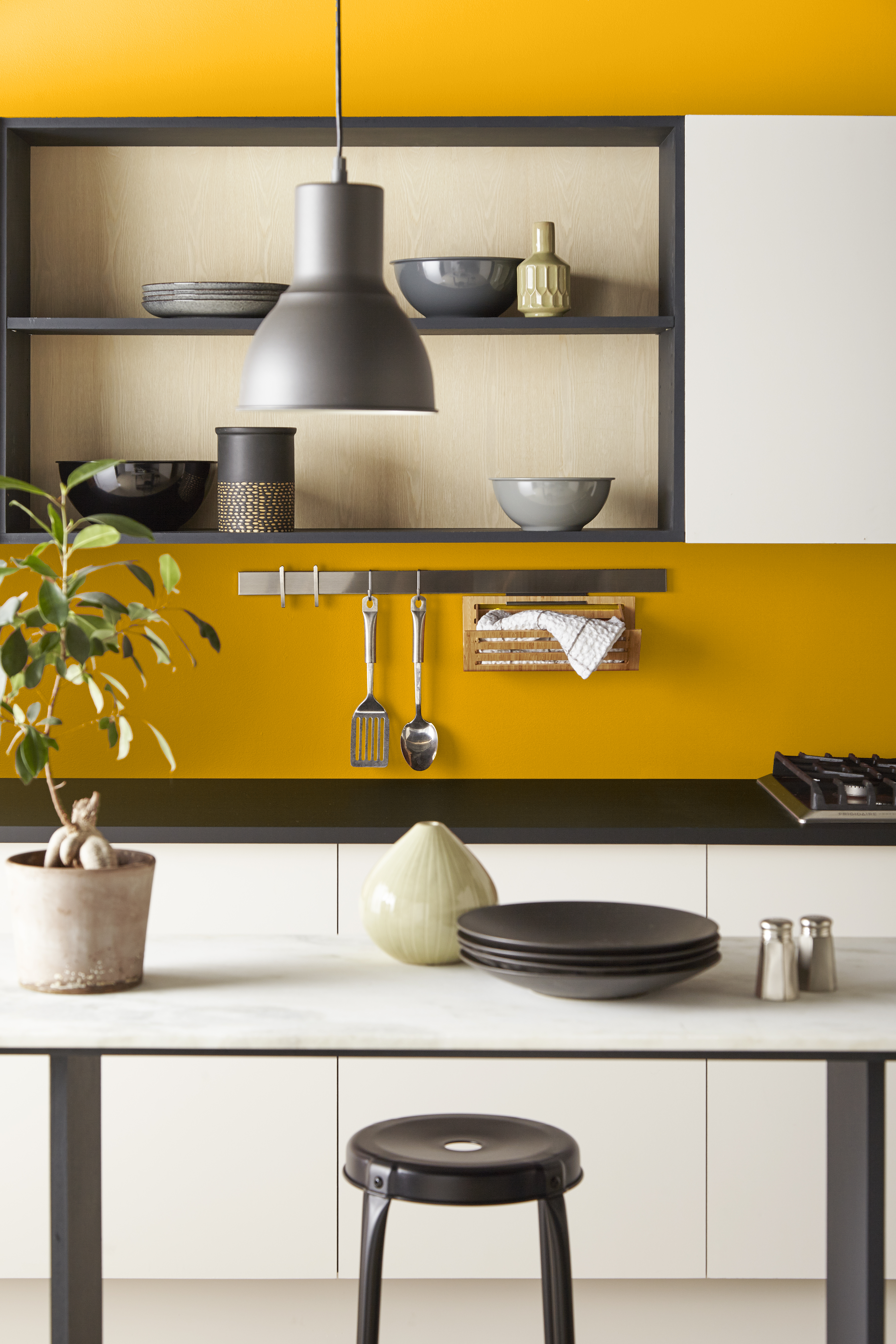 A kitchen with a bold yellow wall and cream painted cabinets.