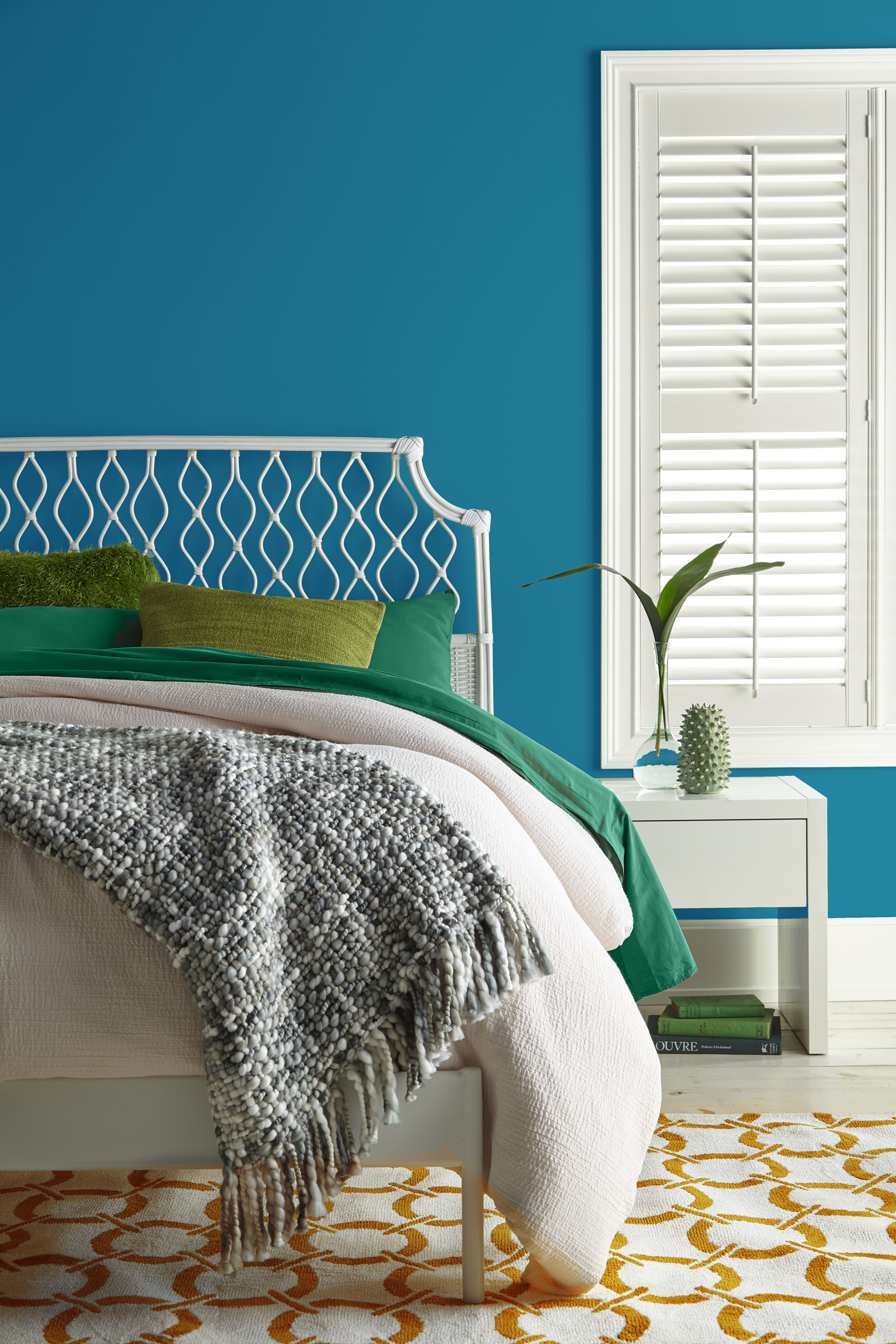 A bedroom with the wall painted in a pure, dark blue hue with linens in green and cream tones.