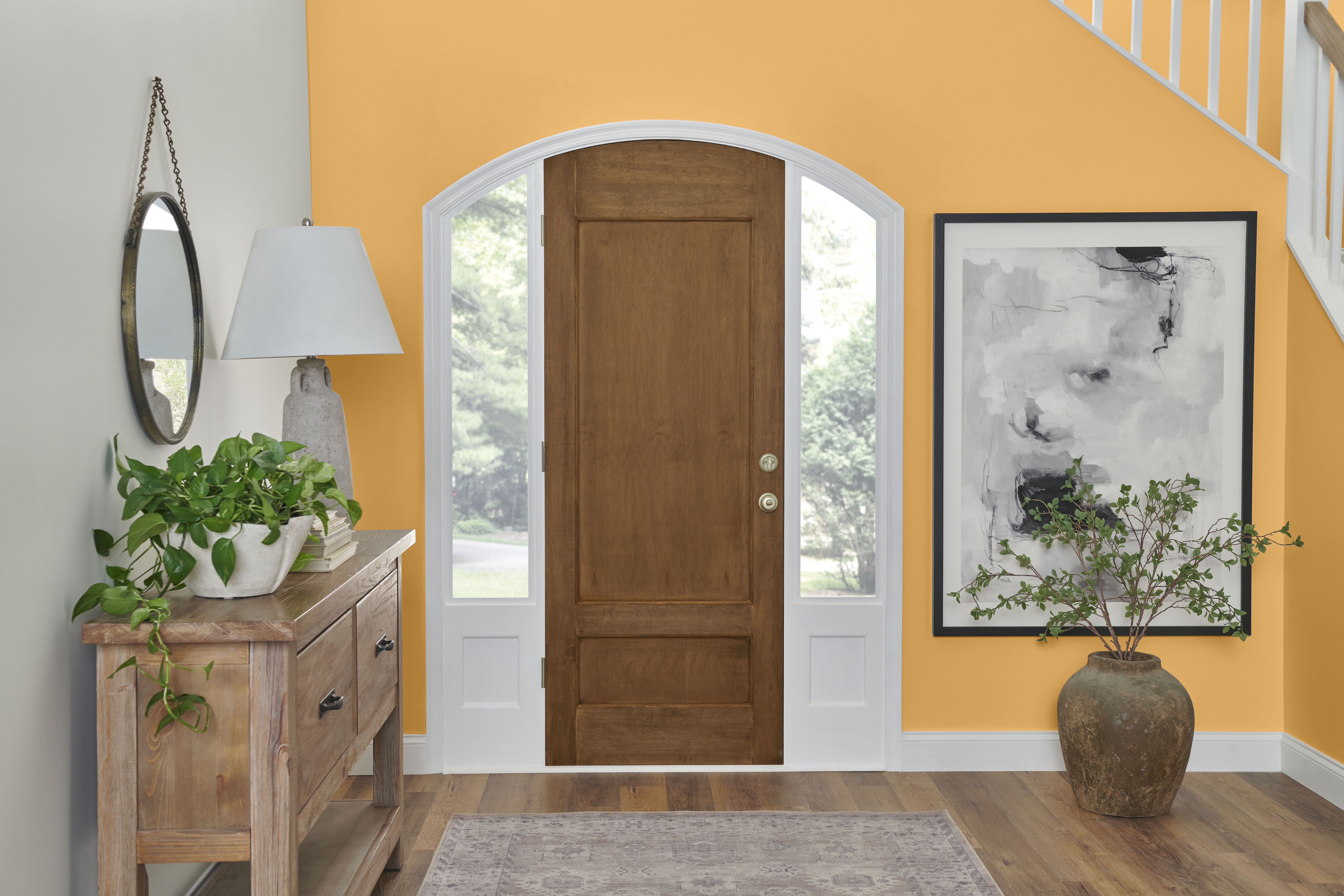 A foyer-entry of a home with a wooden front door and white walls, featuring two accent walls painted in Jackfruit yellow, adding a vibrant and welcoming contrast to the neutral space.