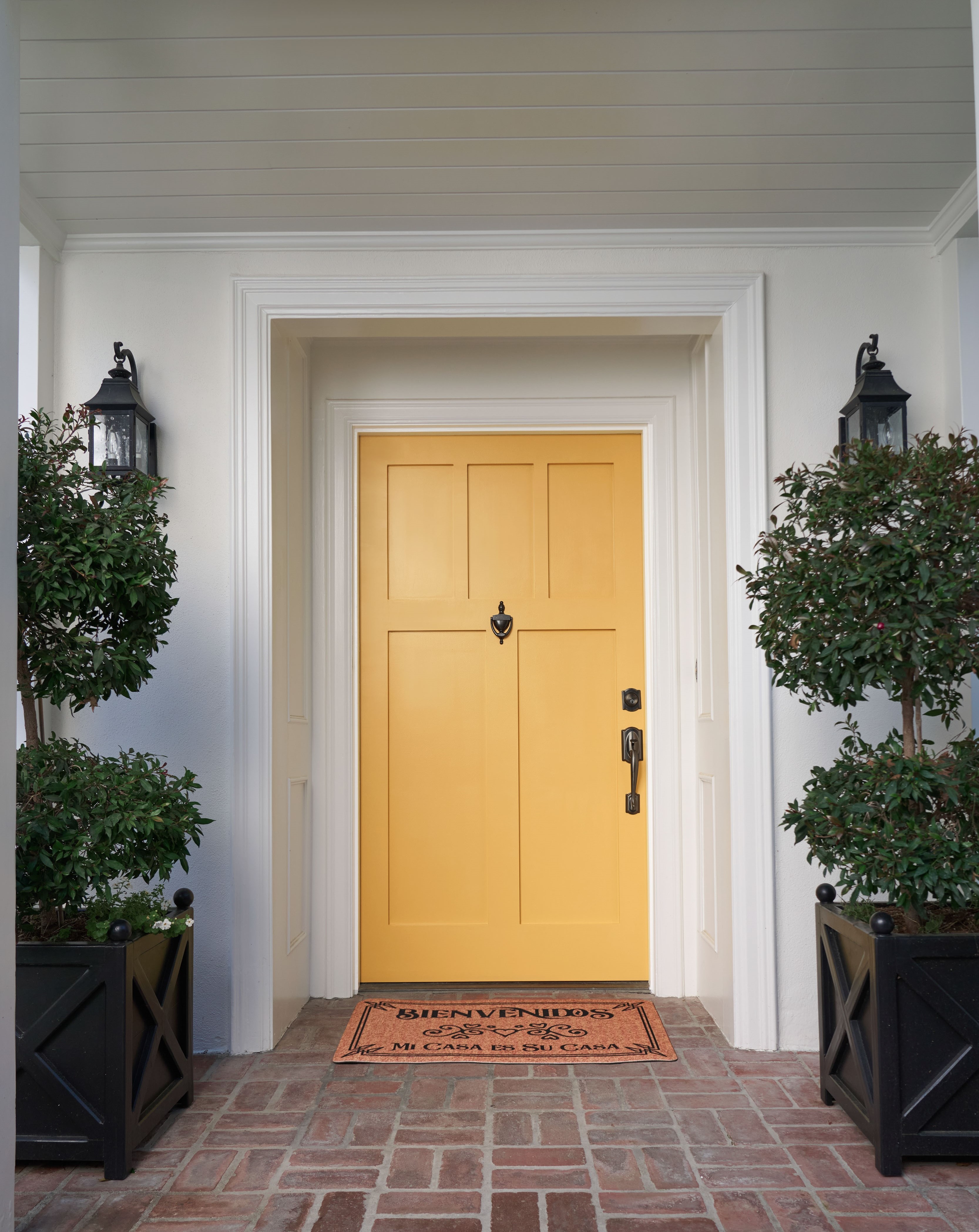 The front entrance of a white home exterior featuring a vibrant yellow door, creating a bold and welcoming focal point against the clean, neutral exterior.