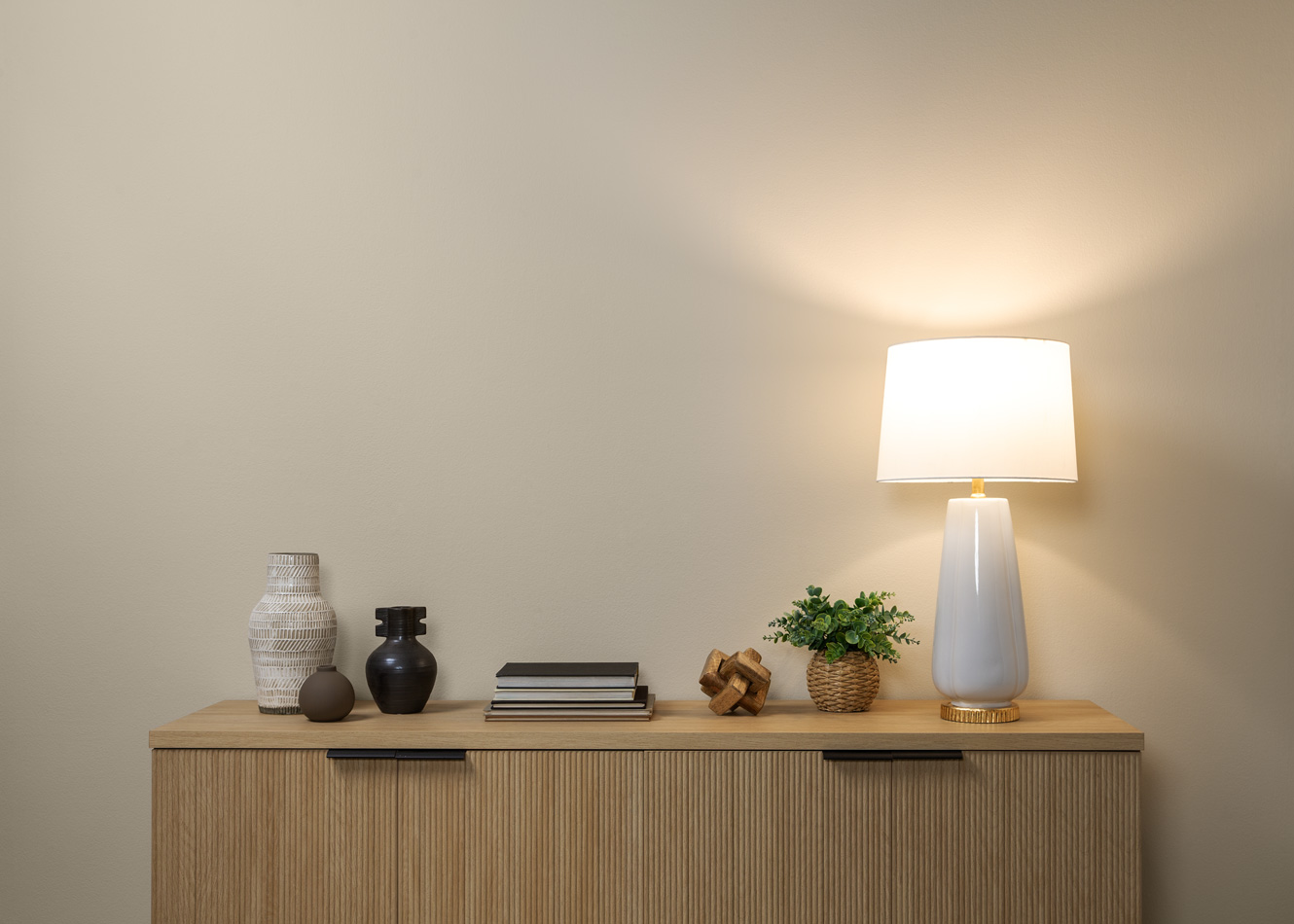Image shows a minimalist, modern stand up against a beige wall. There is a lamp set up with true white lighting.