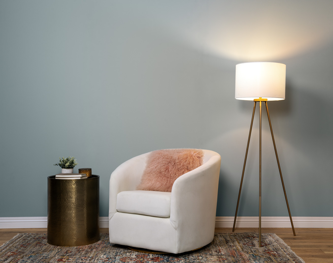 Image displaces a cozy and stylish reading nook, wall is painted in a soft blue grey colour. There is a lamp on with warm lighting.