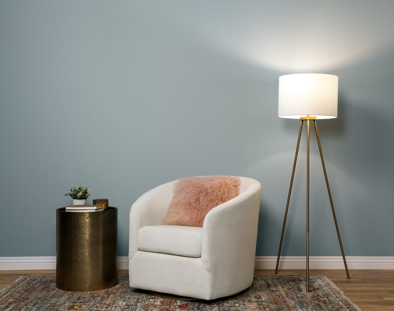 Image displaces a cozy and stylish reading nook, wall is painted in a soft blue grey colour. There is a lamp on with true white lighting.