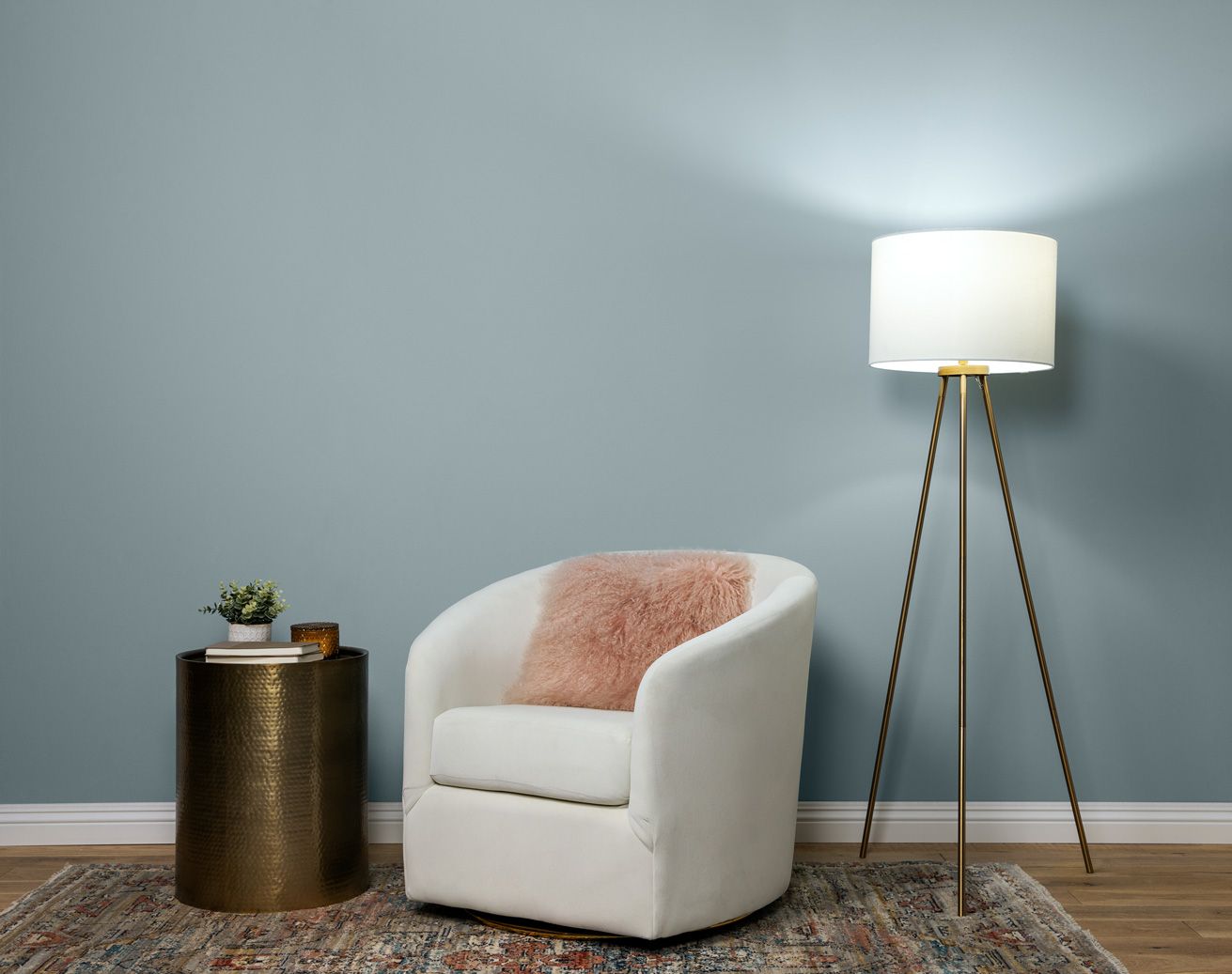 Image displaces a cozy and stylish reading nook, wall is painted in a soft blue grey colour. There is a lamp on with daylight lighting.