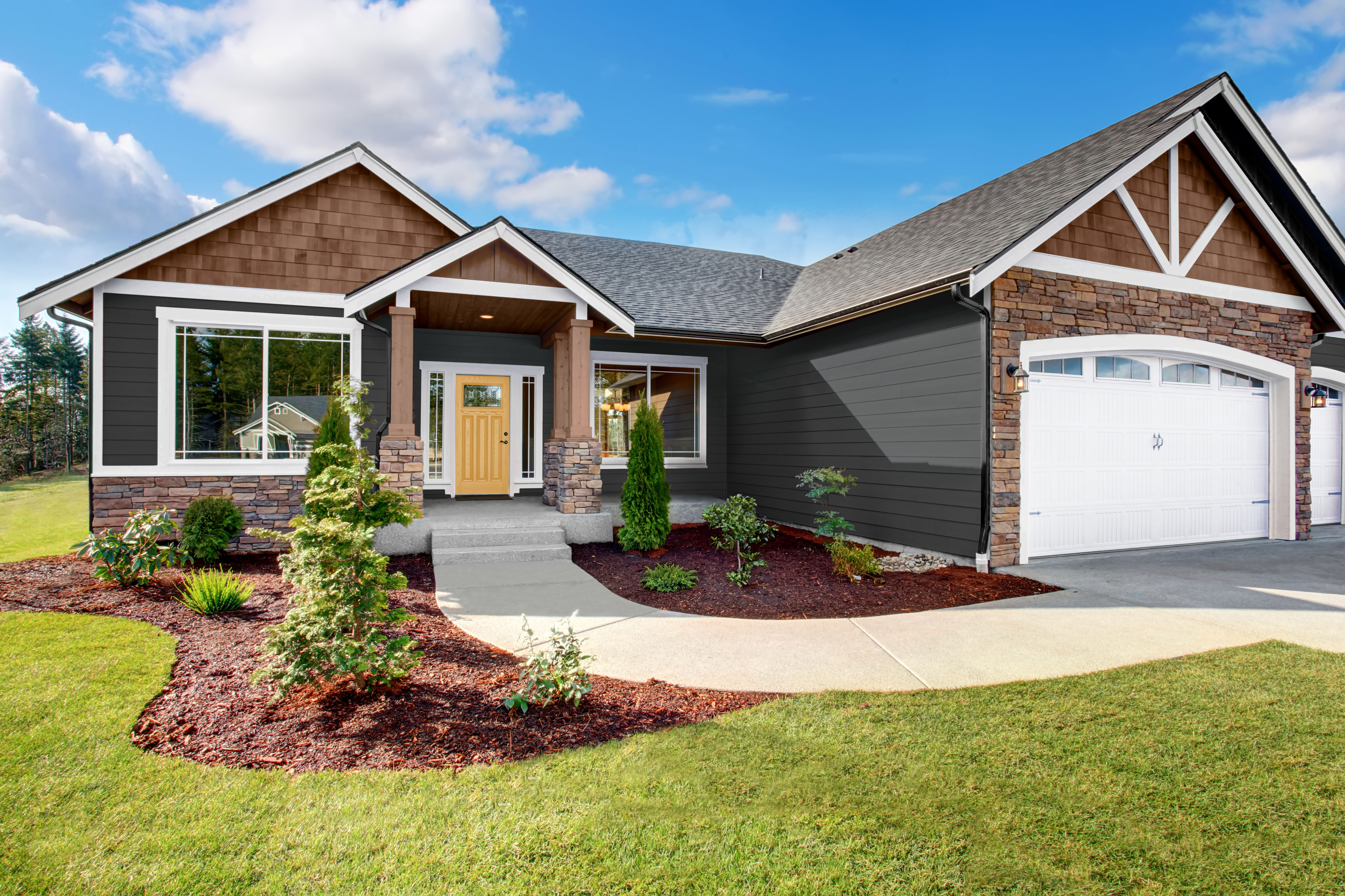 A Ranch-style Craftsman home painted in dark charcoal gray with crisp white trim, featuring natural wood-tone shingles and stone accents. A bright yellow front door adds a cheerful contrast, bringing warmth and personality to the classic exterior.