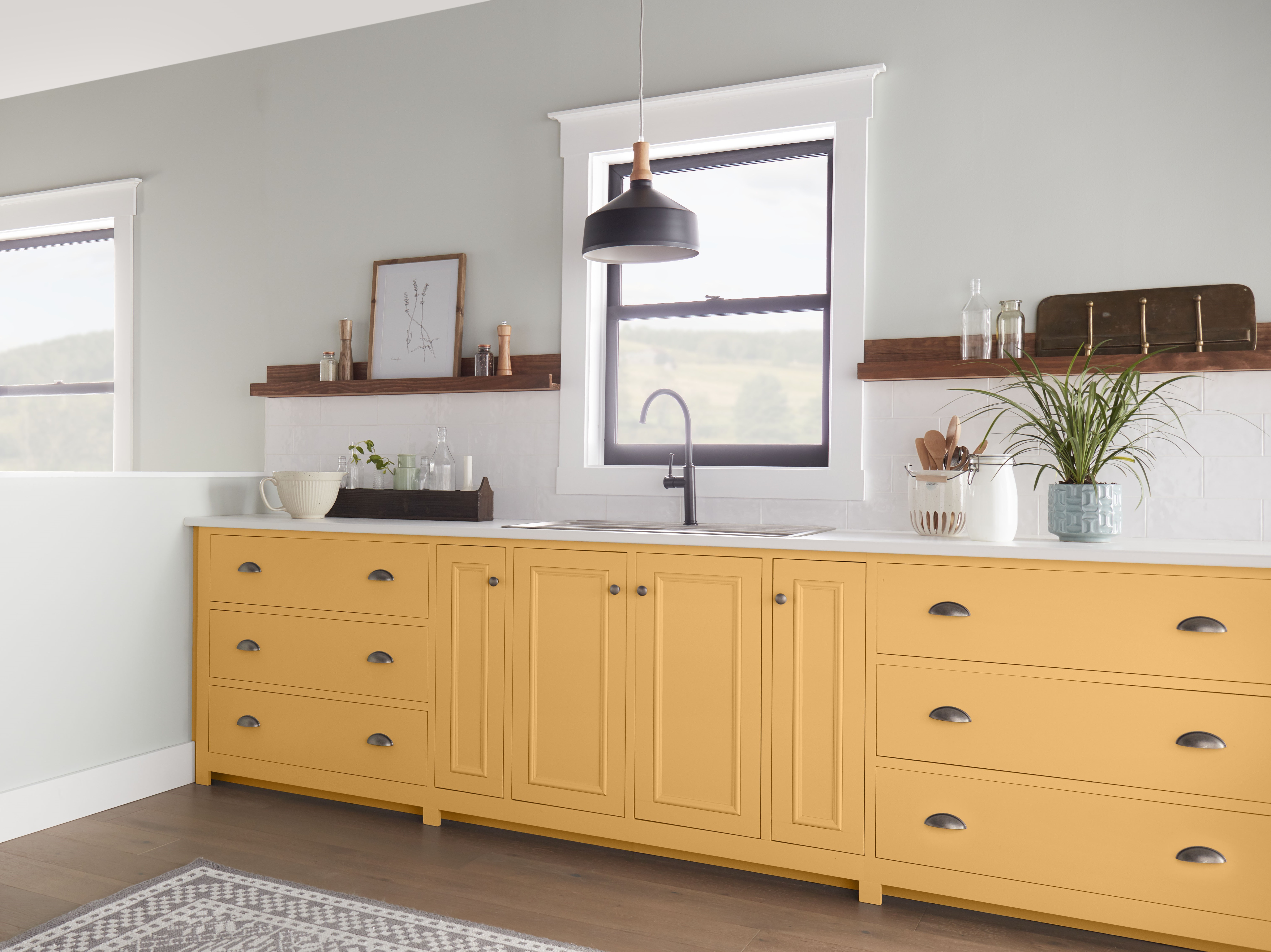 A modern farmhouse kitchen with lower cabinets painted in Jackfruit, natural wood floating shelves, vintage-style hardware, and soft gray-green walls creates a warm, inviting space with a blend of rustic charm and contemporary style.