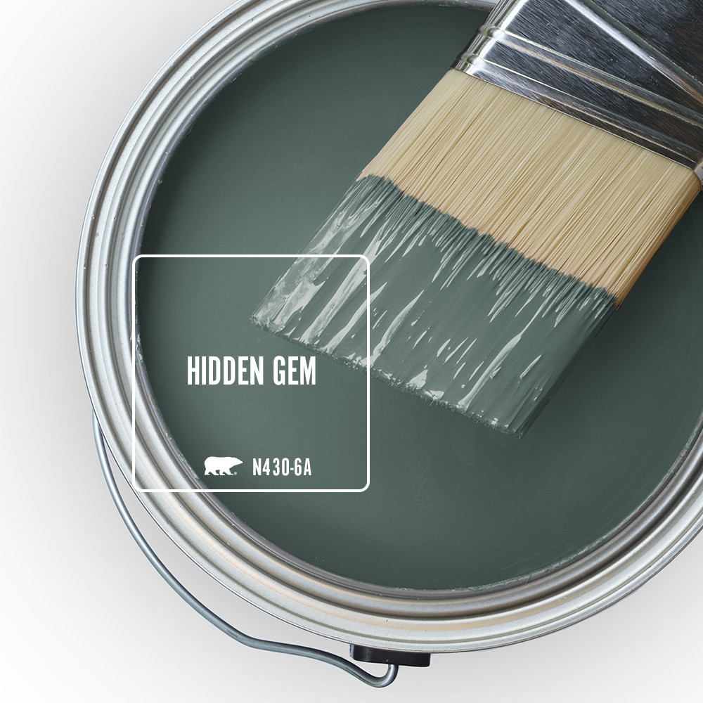 The top view of an open paint can, the colour inside the can is Hidden Gem. There is a half-dipped paint brush resting on top of the can rim.