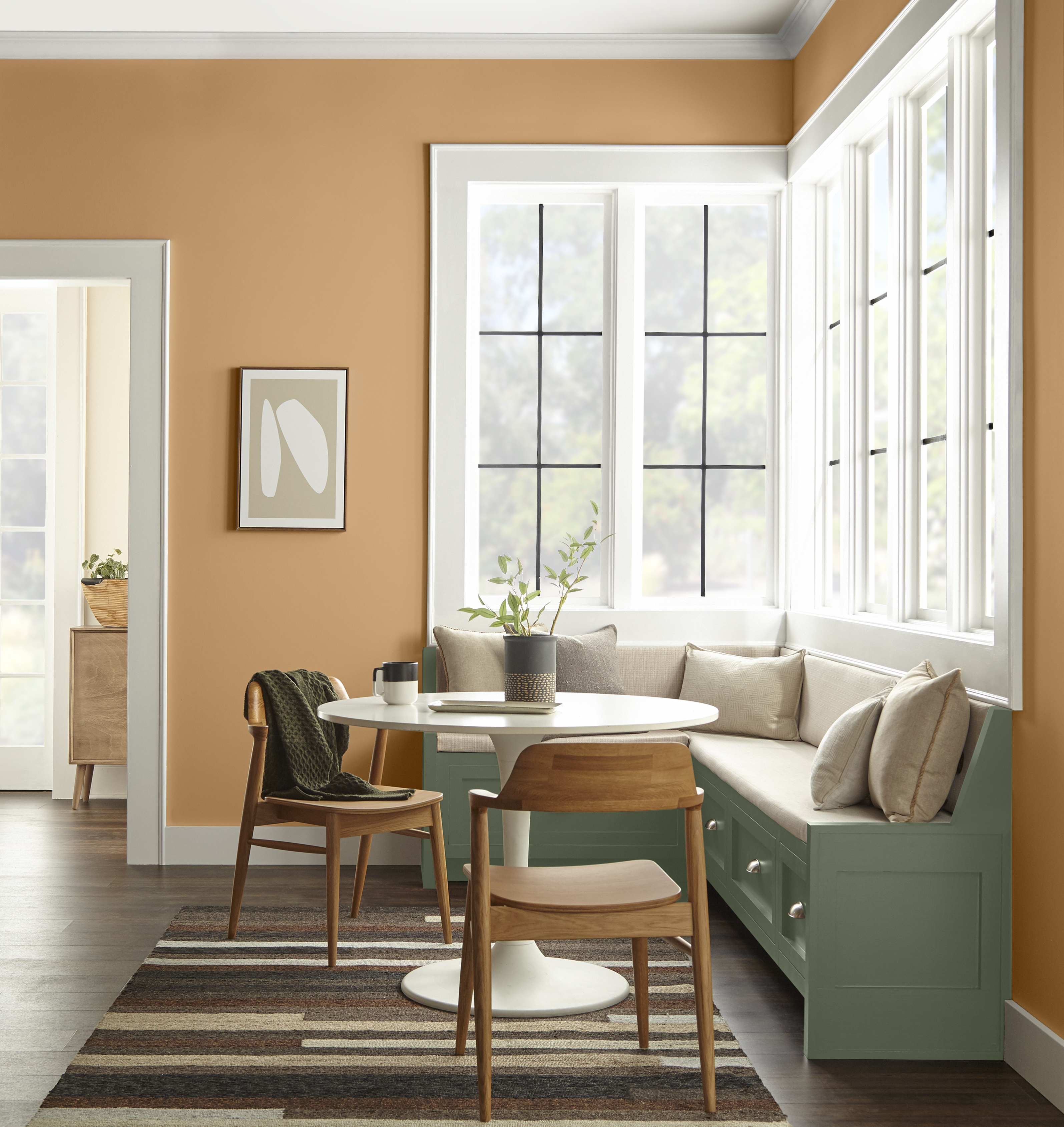 A kitchen nook with walls in a caramel orange hue and a seating bench painted in deep green.