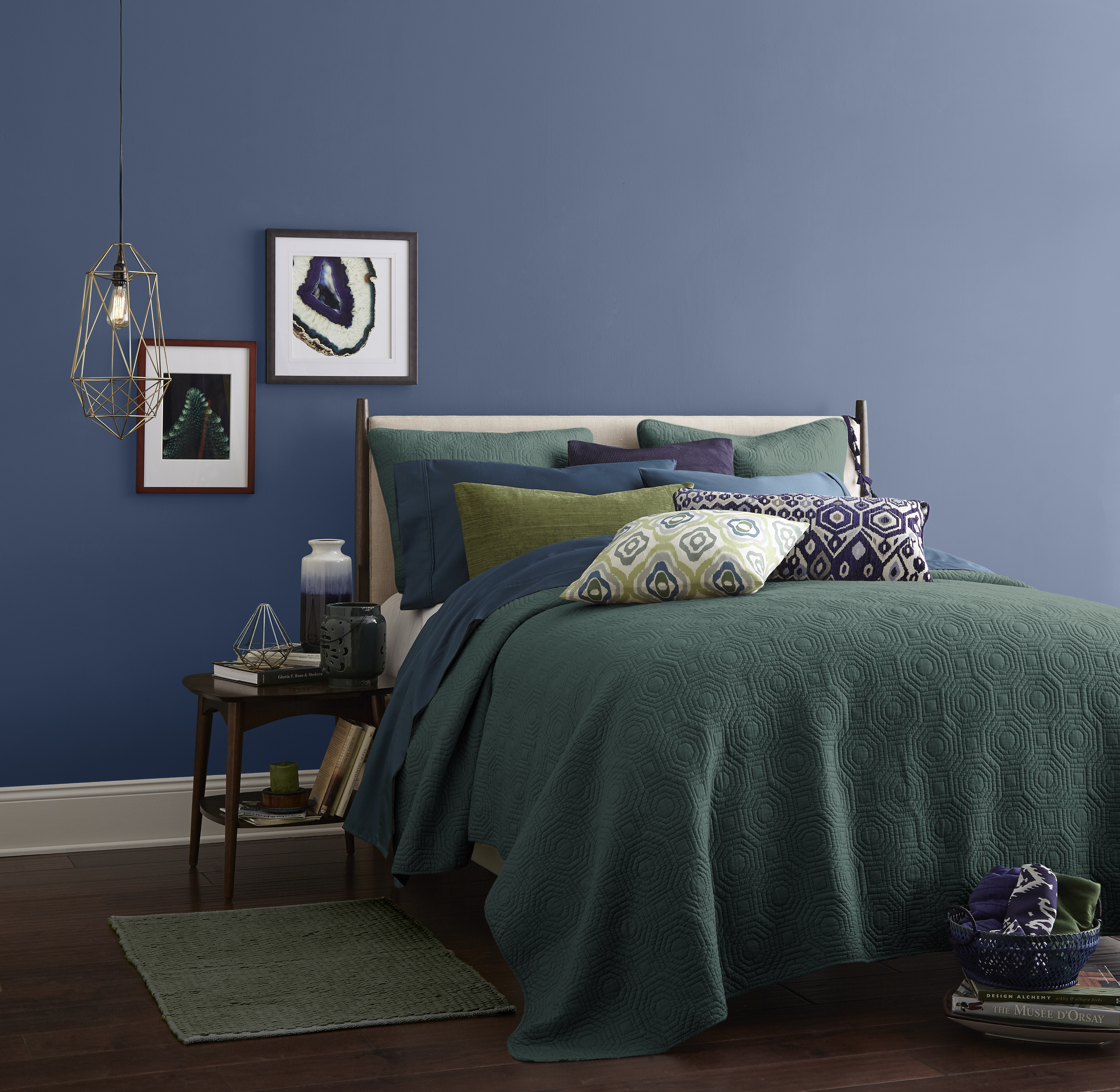 A bedroom with walls painted in a calming blue hue painted on the walls. Bedding is in green, blue and purple jewel tones.