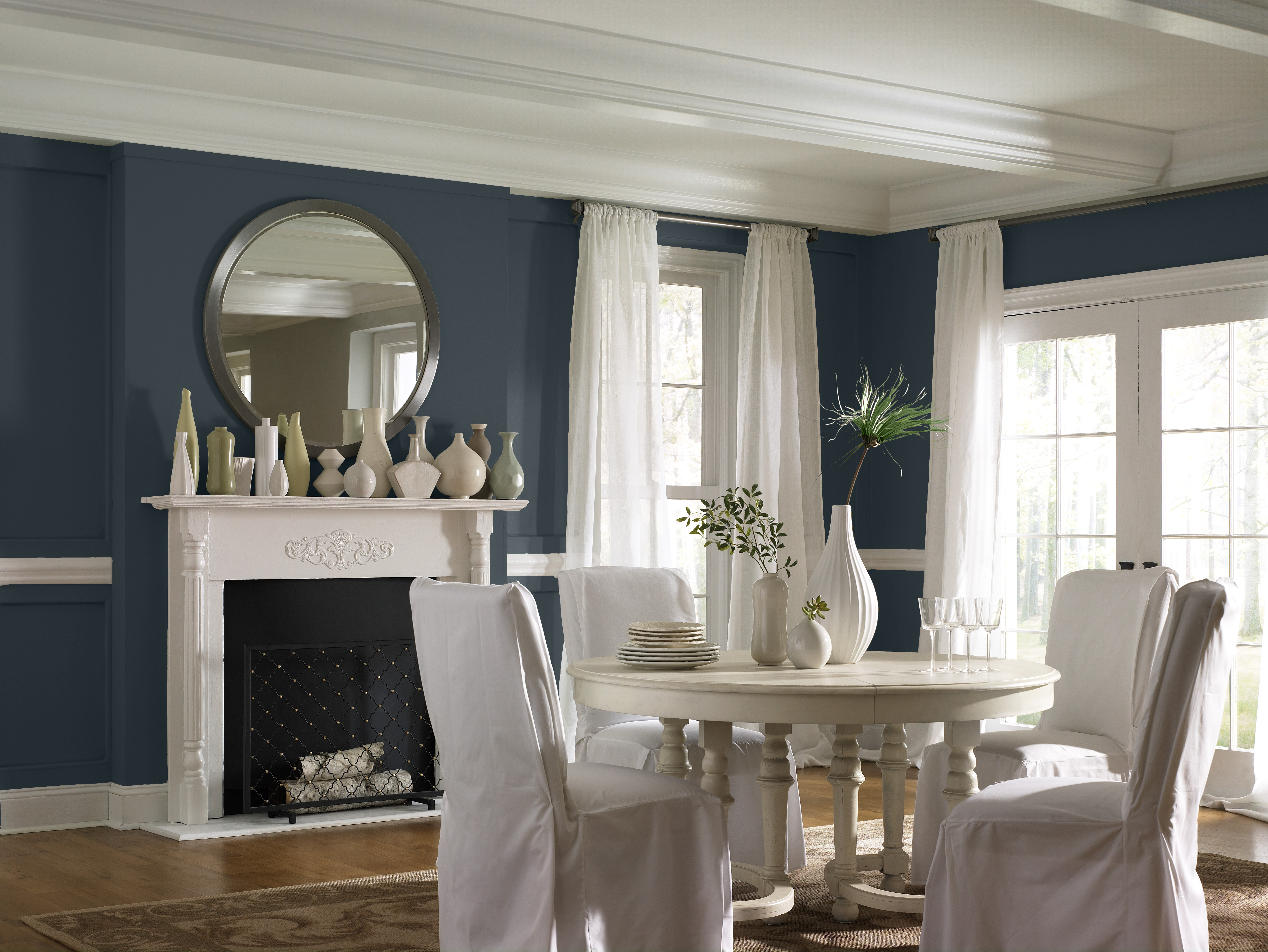 A dining room with a calming green-black tone on the walls and warm fireplace painted in a crisp white.