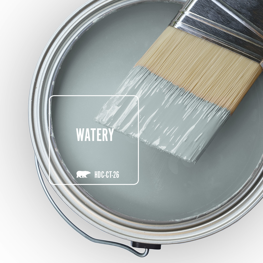An open paint can filled with Behr Watery HDC-CT-26, a soft blue-green colour, with a paintbrush resting across the top coated in the same paint.