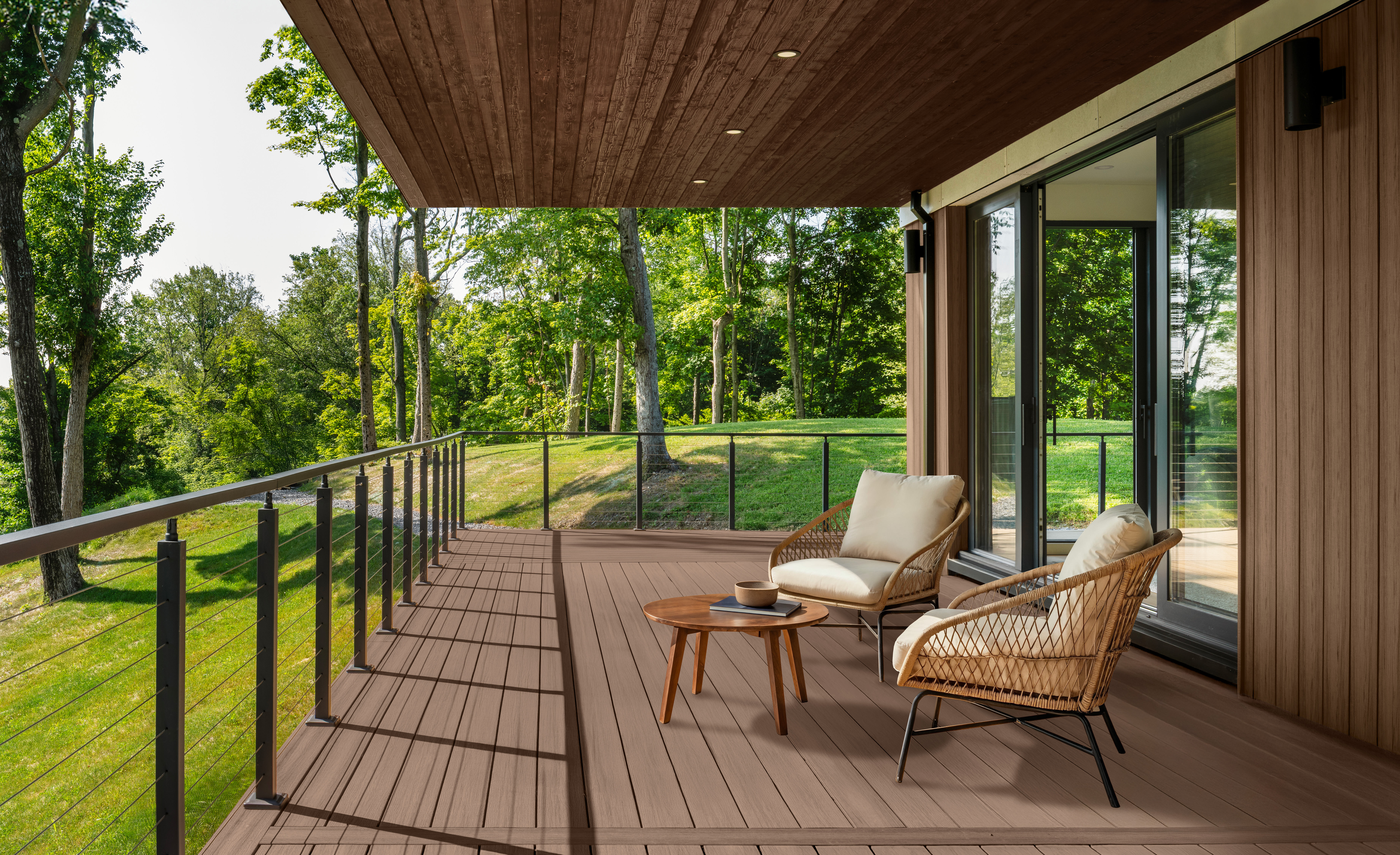 A covered outdoor deck with two different wood stain colours.  Taupe is the wood stain colour of the floor and wood ceiling is a colour called Chocolate. The deck is furnished with two lounge chairs and a small table, overlooking a grassy landscape with trees.