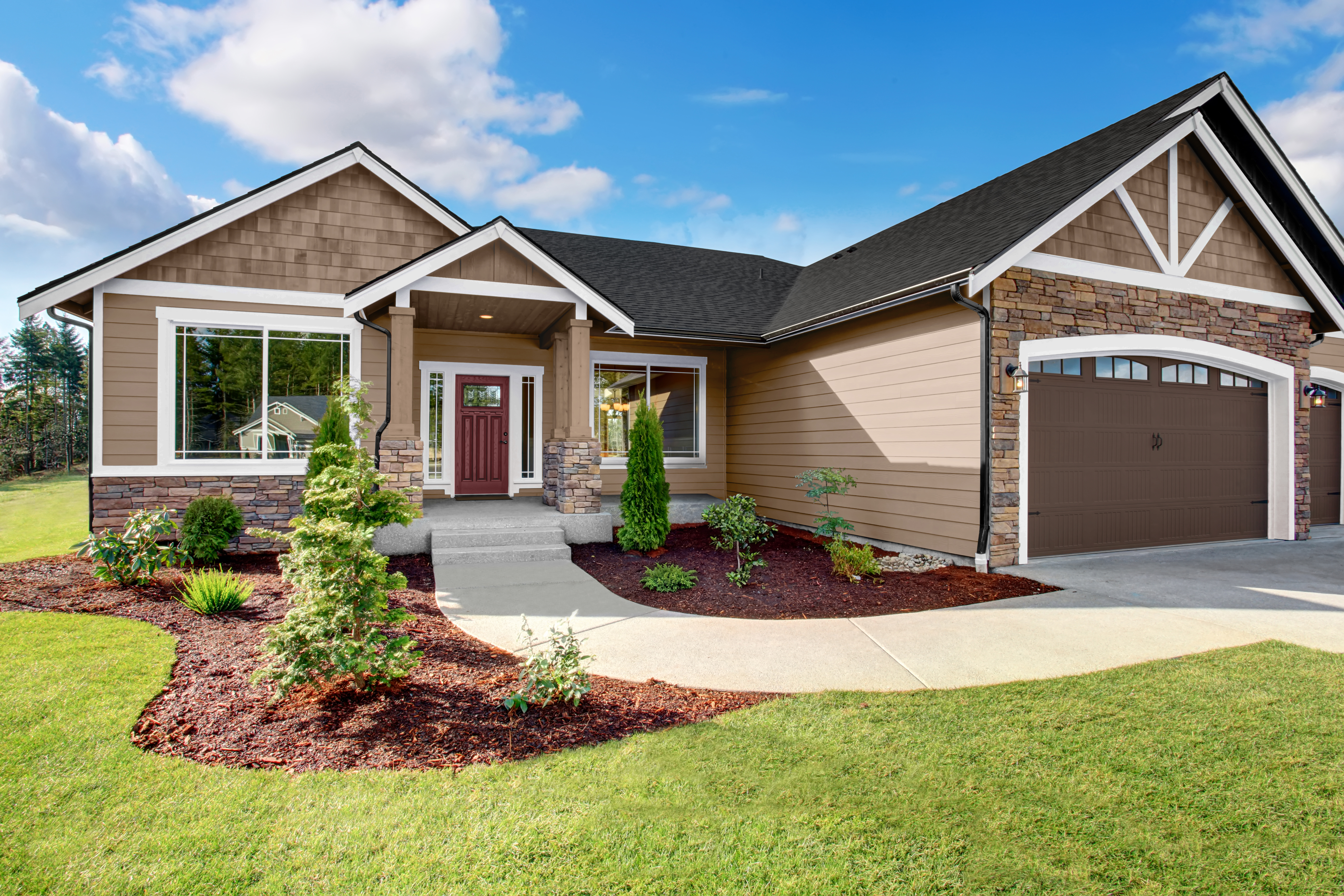A Craftsman-style home exterior with Taupe siding, white trim accents, stone details, and a landscaped front yard leading to a covered entry and garage.